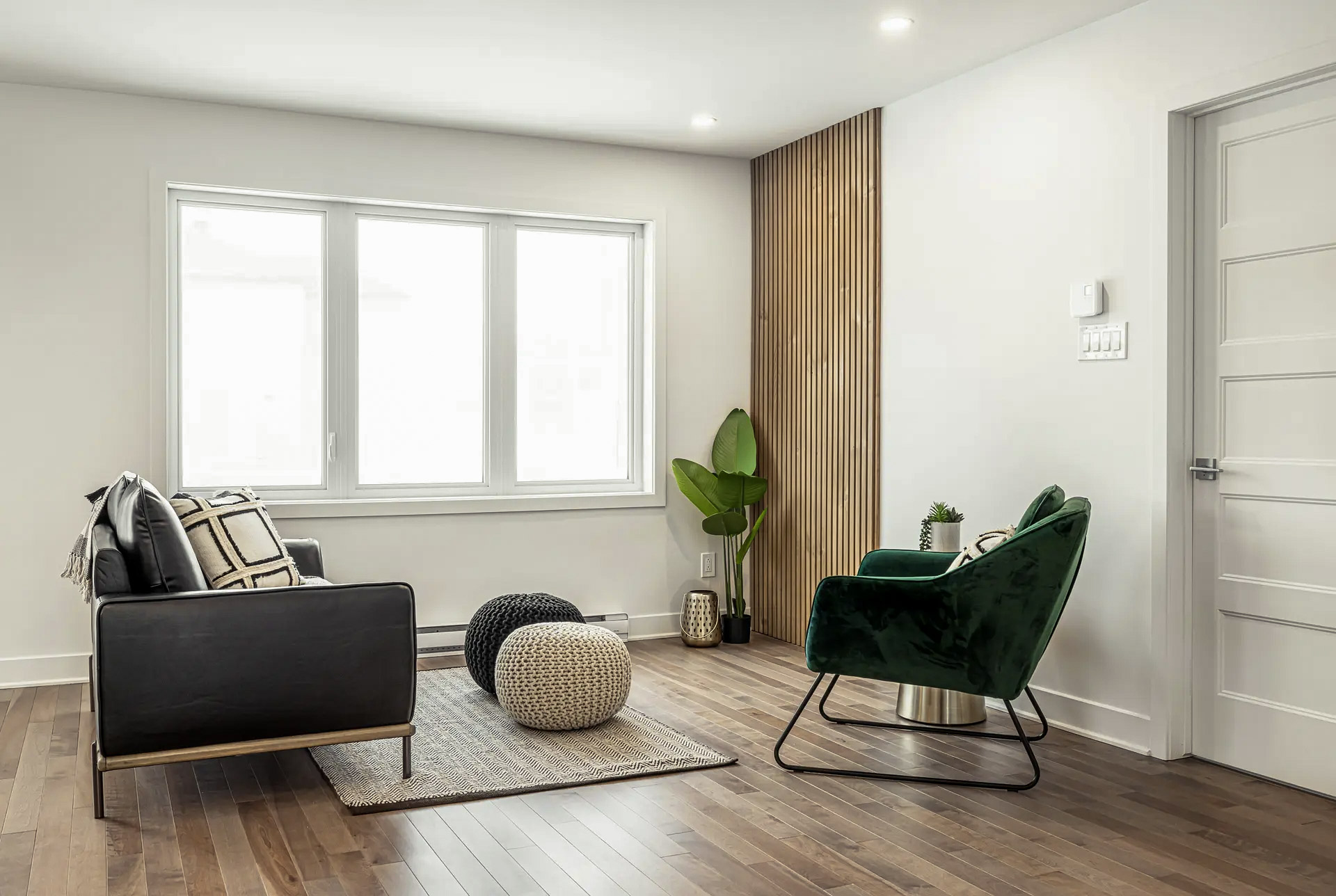 Minimalist living room with modern furniture, green velour armchair, wood-pannelled accent wood, and light brown wood floors