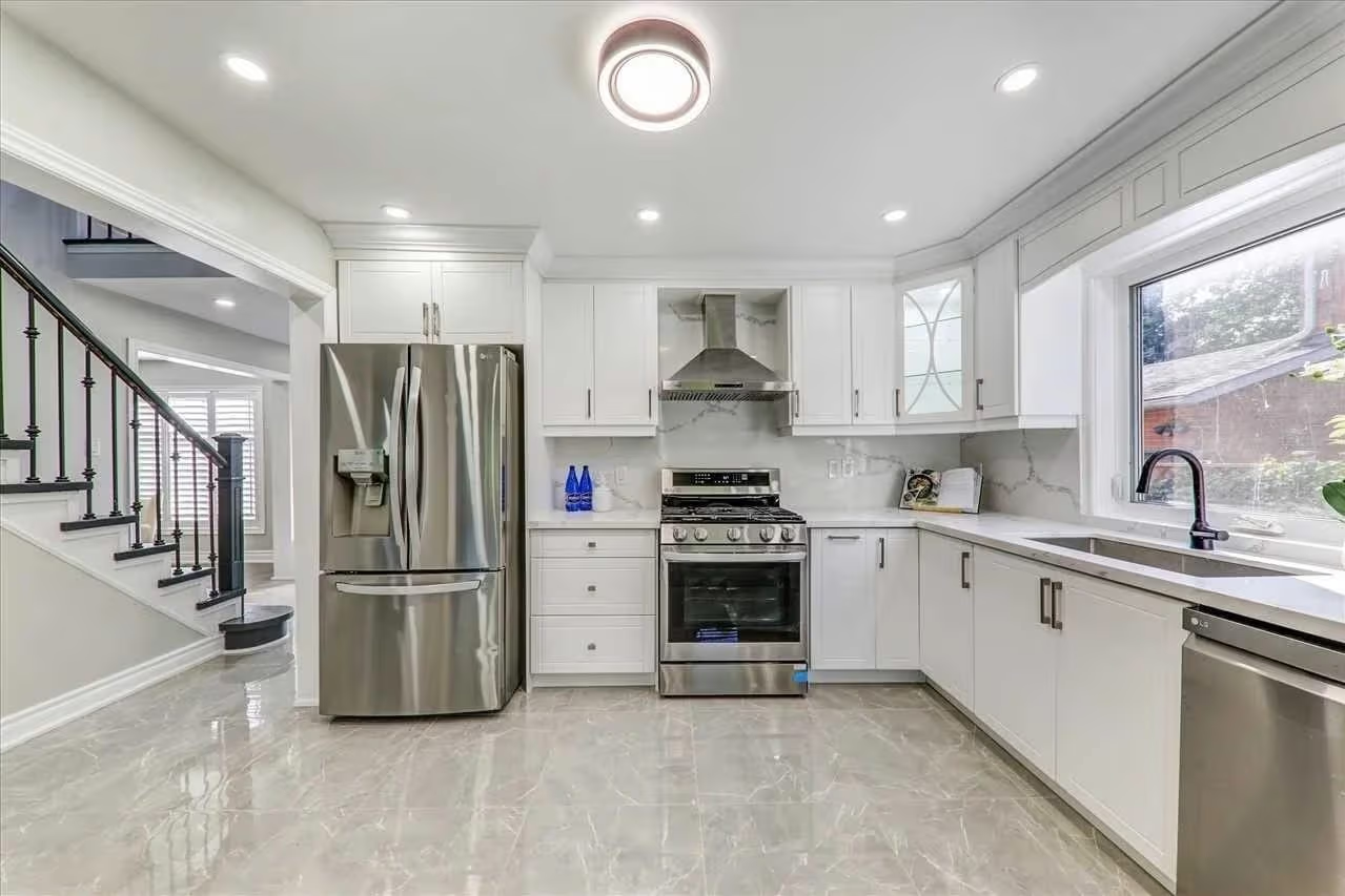 Bright modern kitchen with white cabinetry, marble-look countertops, stainless steel appliances, a large window above the sink, and glossy ceramic tile flooring.