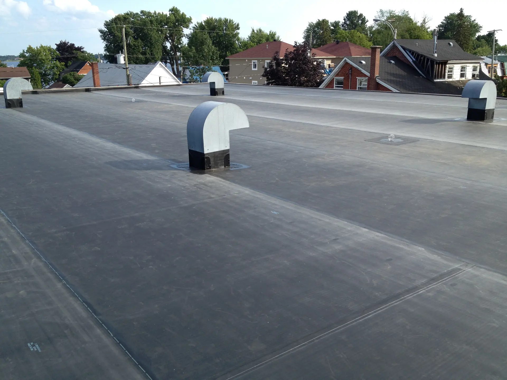 Black flat roof with elastomeric membrane, aligned ventilation vents on residential building in urban area