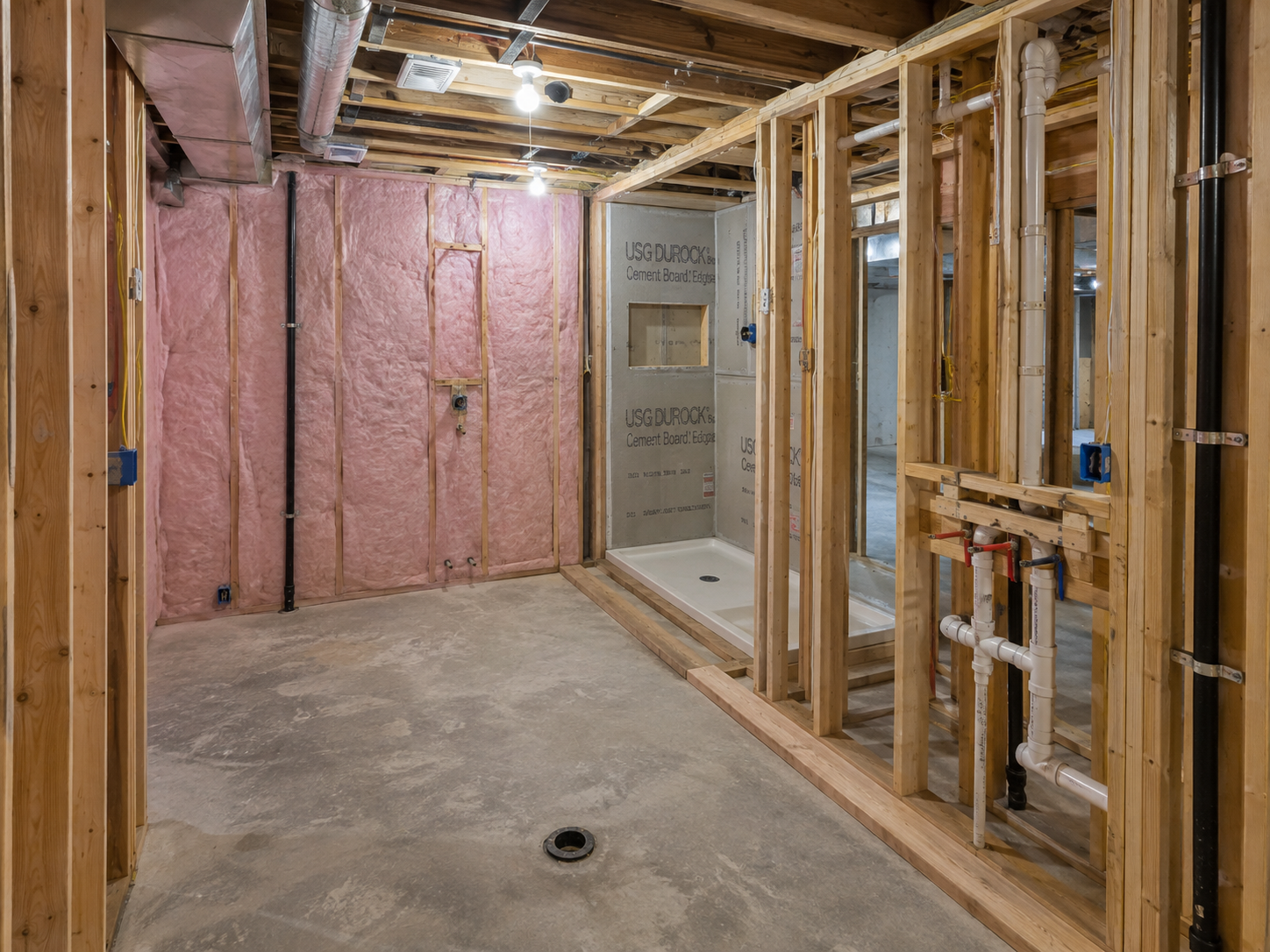 Salle de bain de sous-sol en construction avec ossature en bois, isolation en fibre de verre, plomberie apparente, conduits de ventilation et base de douche installée