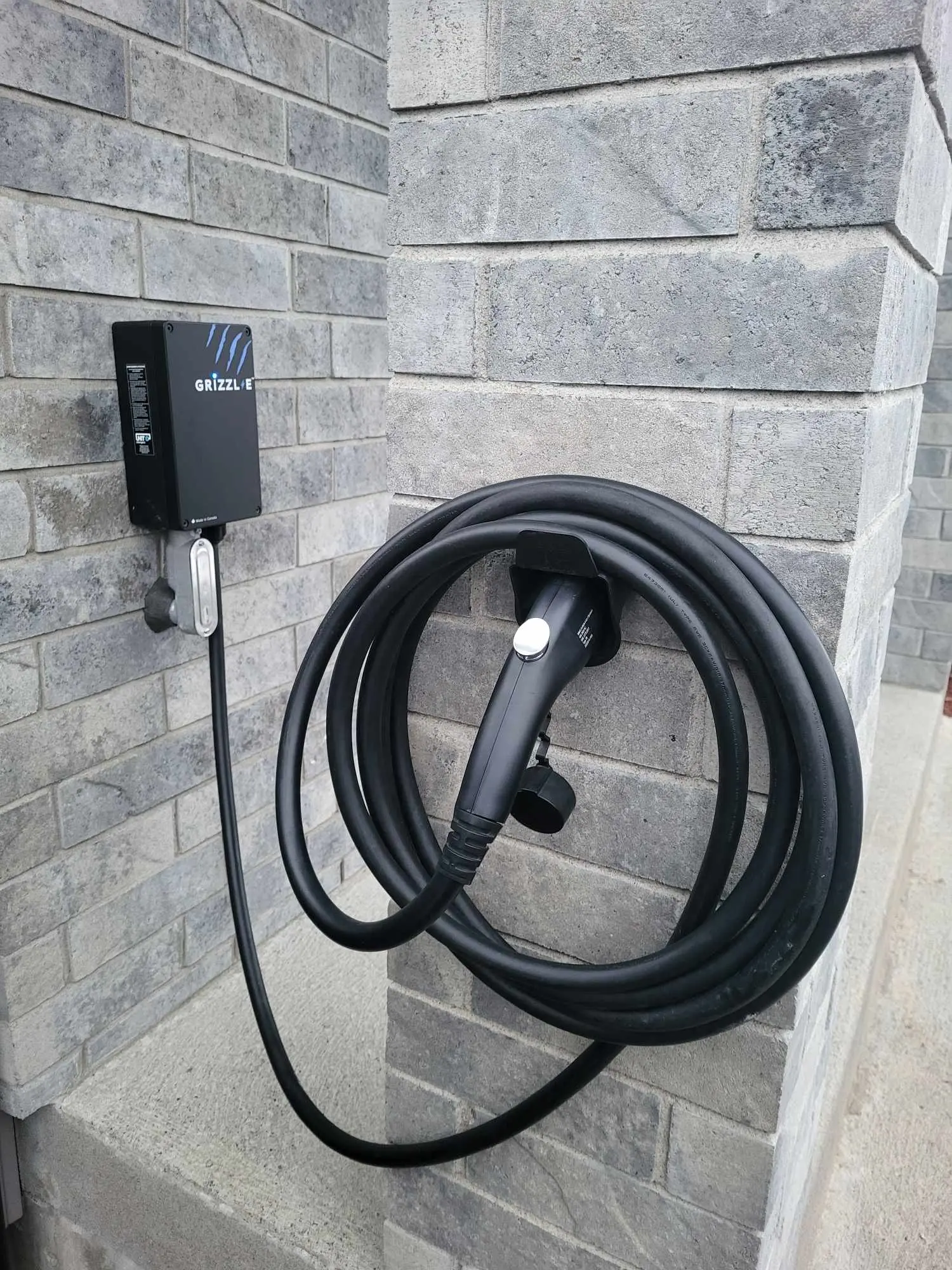 Electric vehicle charging station mounted on brick wall with coiled charging cable outdoors