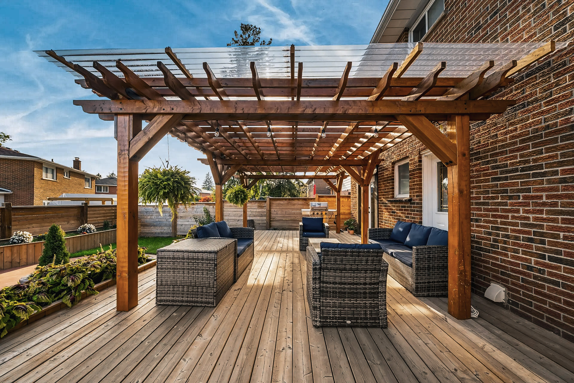 Modern outdoor patio with wooden pergola, rattan furniture, blue cushions, privacy panels and elegant landscaping.