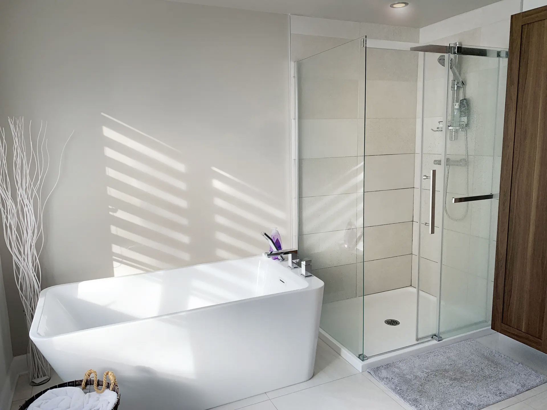 Modern and bright bathroom with white freestanding bathtub, glass shower, beige tiles, wooden furniture, gray carpet and natural light for a refined and warm atmosphere