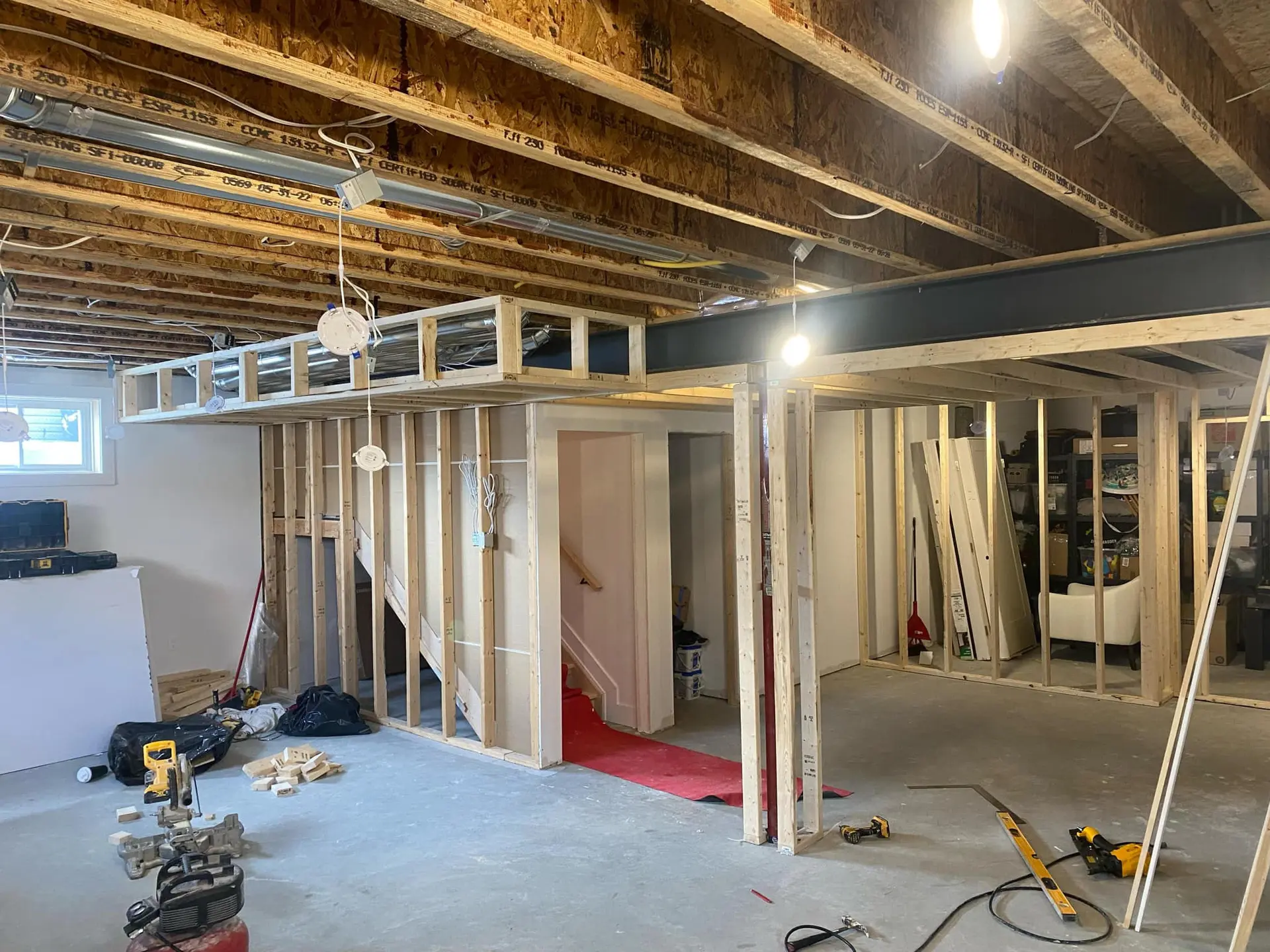 Sous-sol en rénovation avec nouvelle structure de bois, poutre apparente, plafond ouvert, fils électriques et outils de chantier.