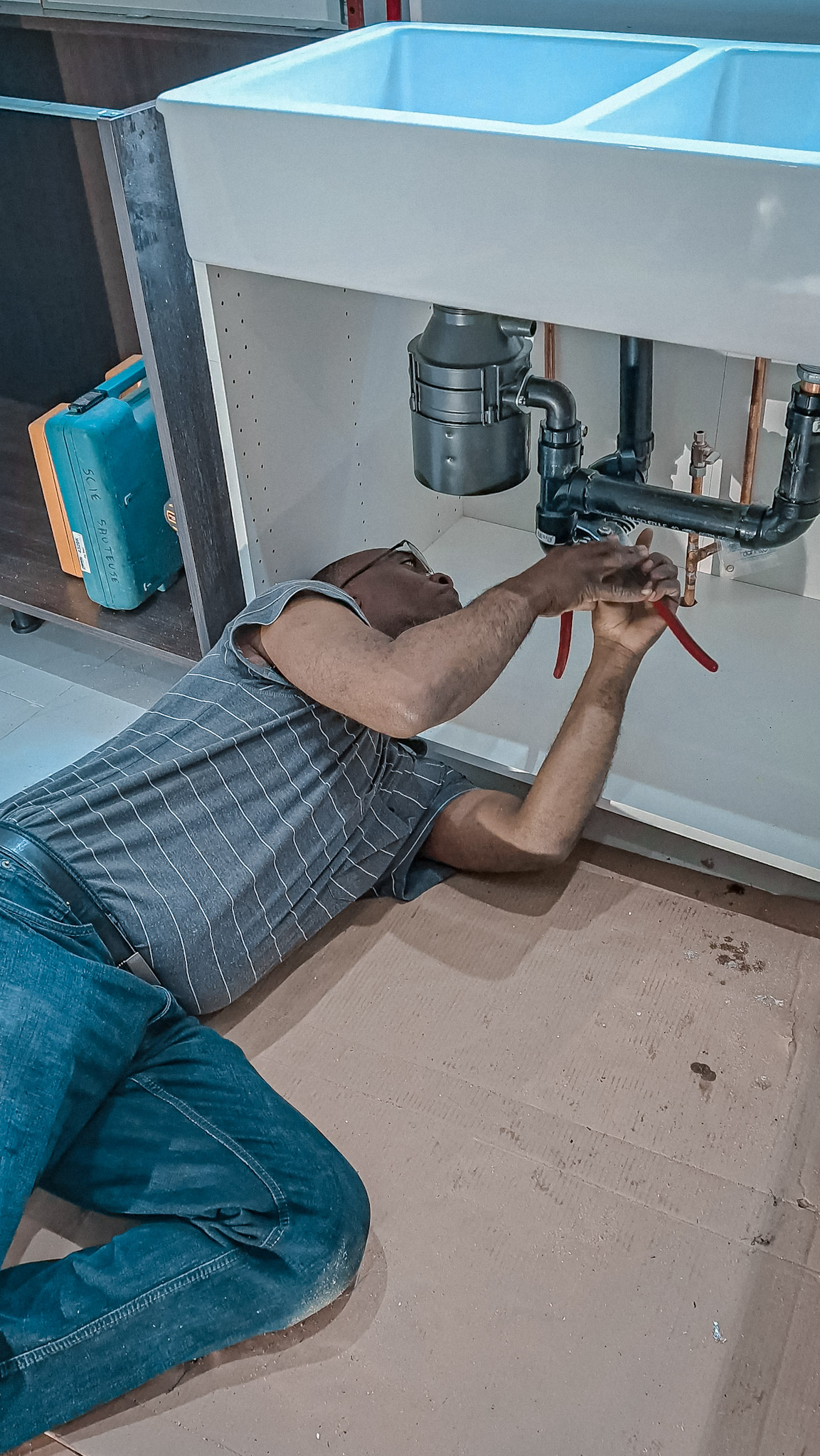 Plombier effectuant le raccordement des tuyaux et du broyeur à déchets sous un évier double pendant des travaux d’installation.