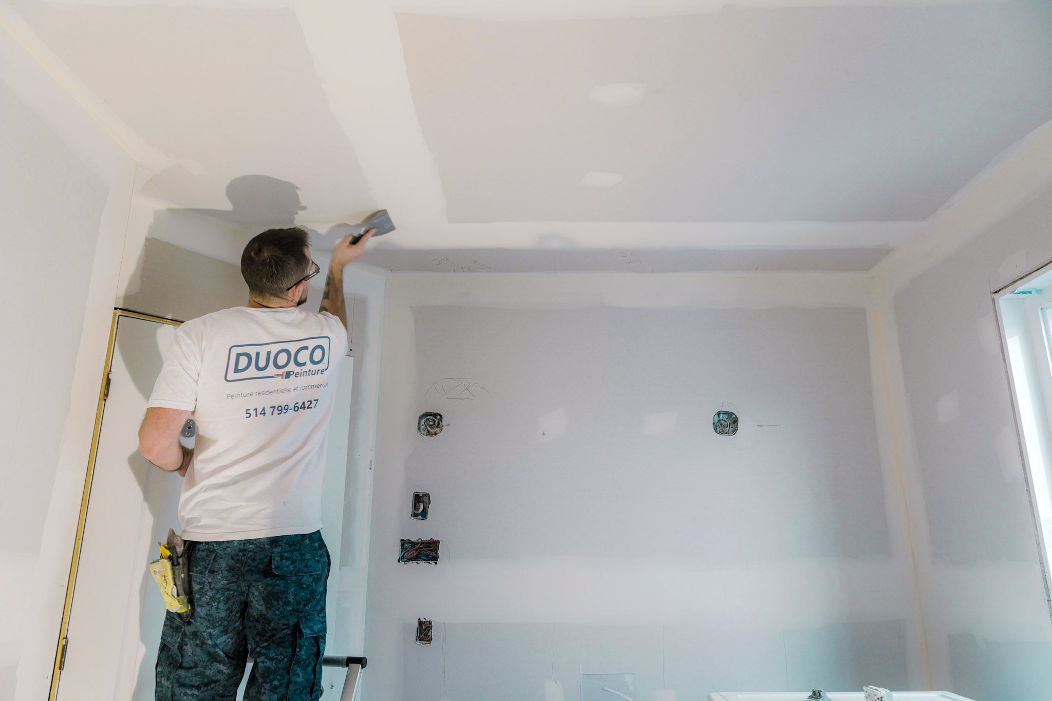 Ouvrier appliquant du composé à joints sur un plafond en plaques de plâtre lors de rénovations intérieures