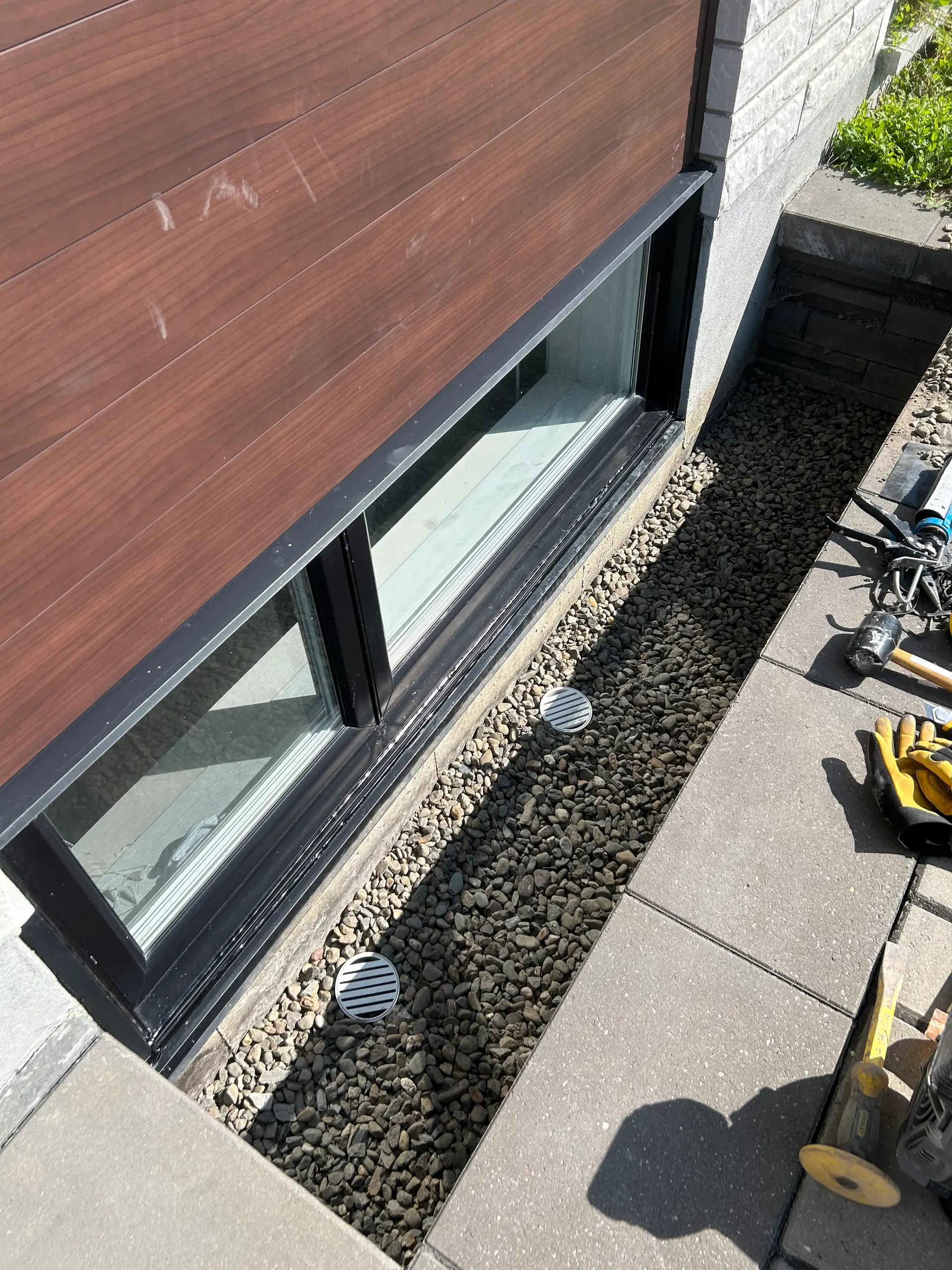 Window well with gravel drainage and protective grates installed at ground level of a basementS