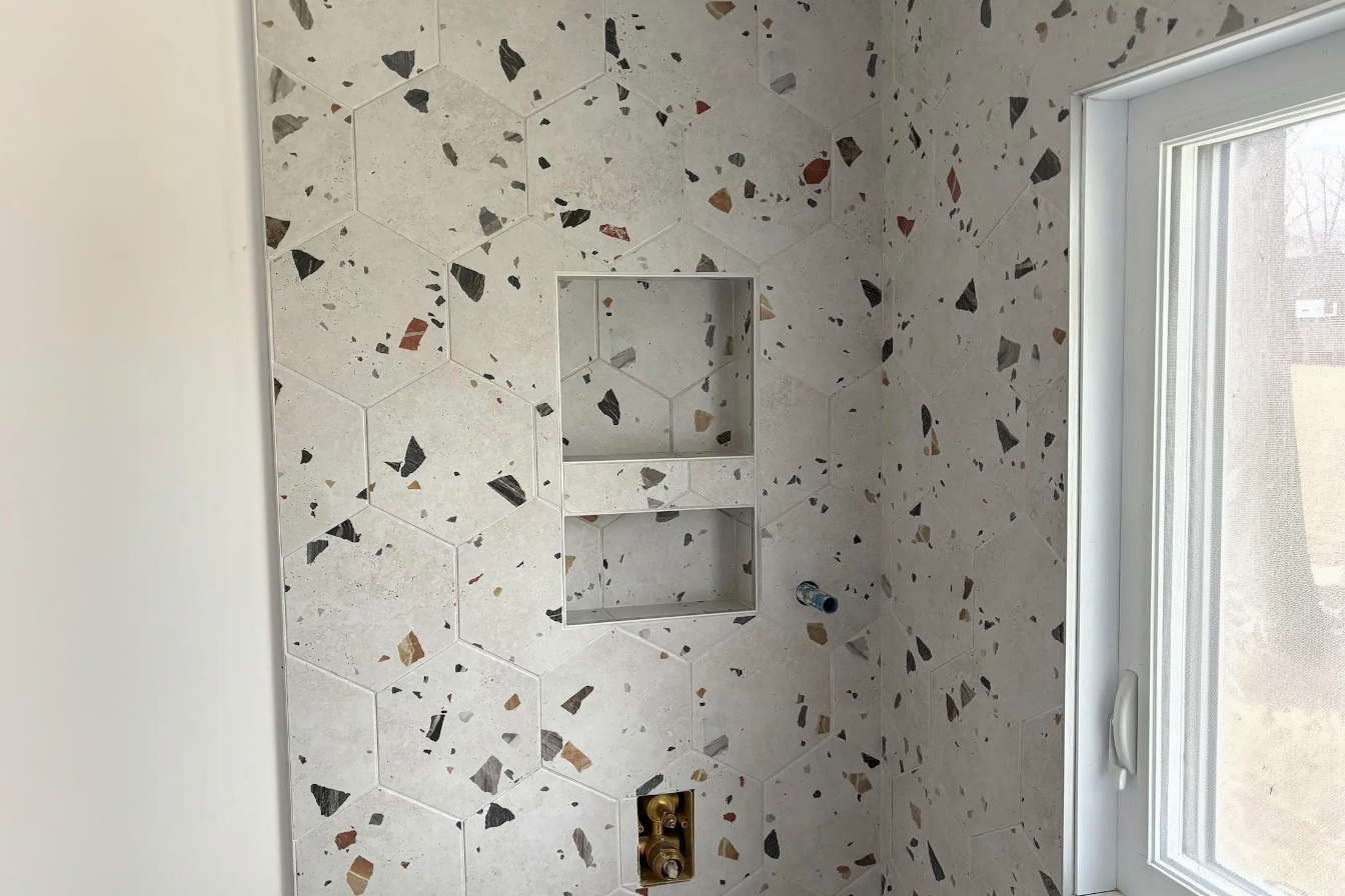 Douche moderne avec carrelage hexagonal effet terrazzo et niche murale intégrée dans une salle de bain lumineuse