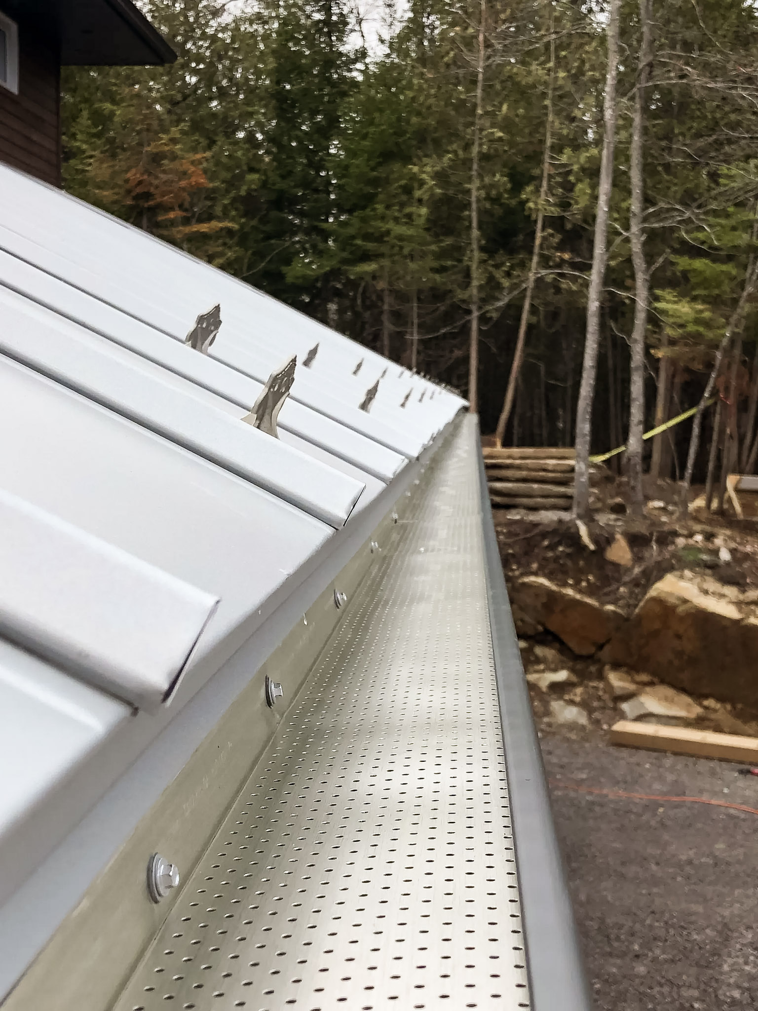 Perforated gutter guard installed along a white metal roof in a wooded setting.