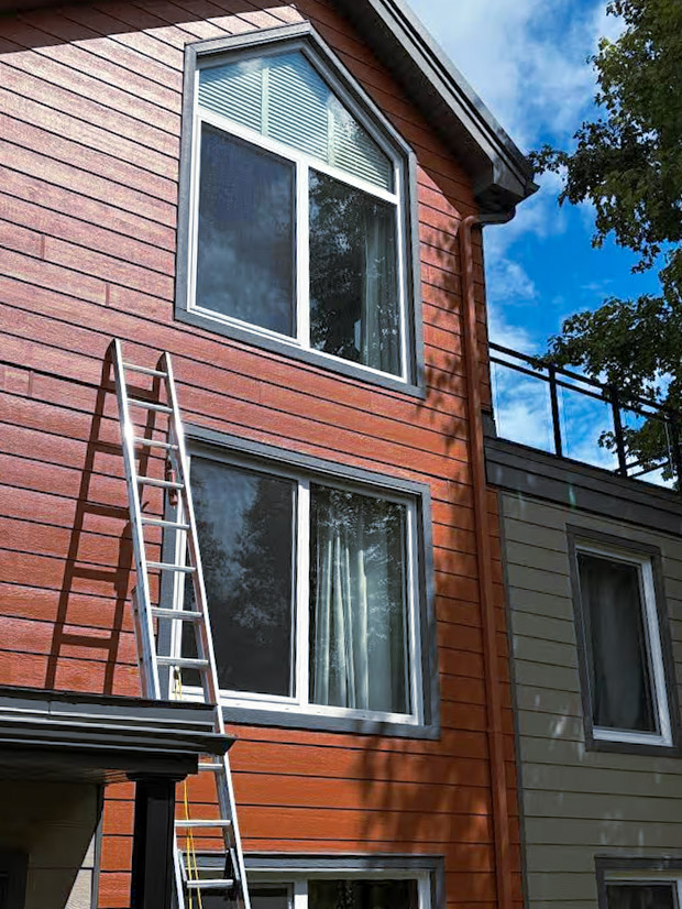 Maison avec revêtement extérieur rouge en déclin horizontal, grandes fenêtres et échelle appuyée pour travaux en façade