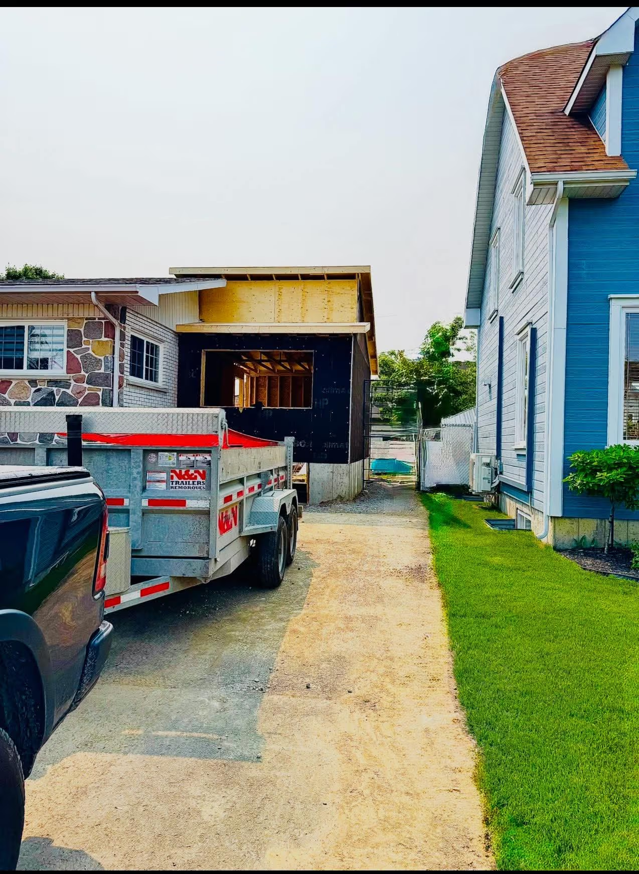Agrandissement de maison en construction avec structure en bois, remorque de chantier et allée résidentielle