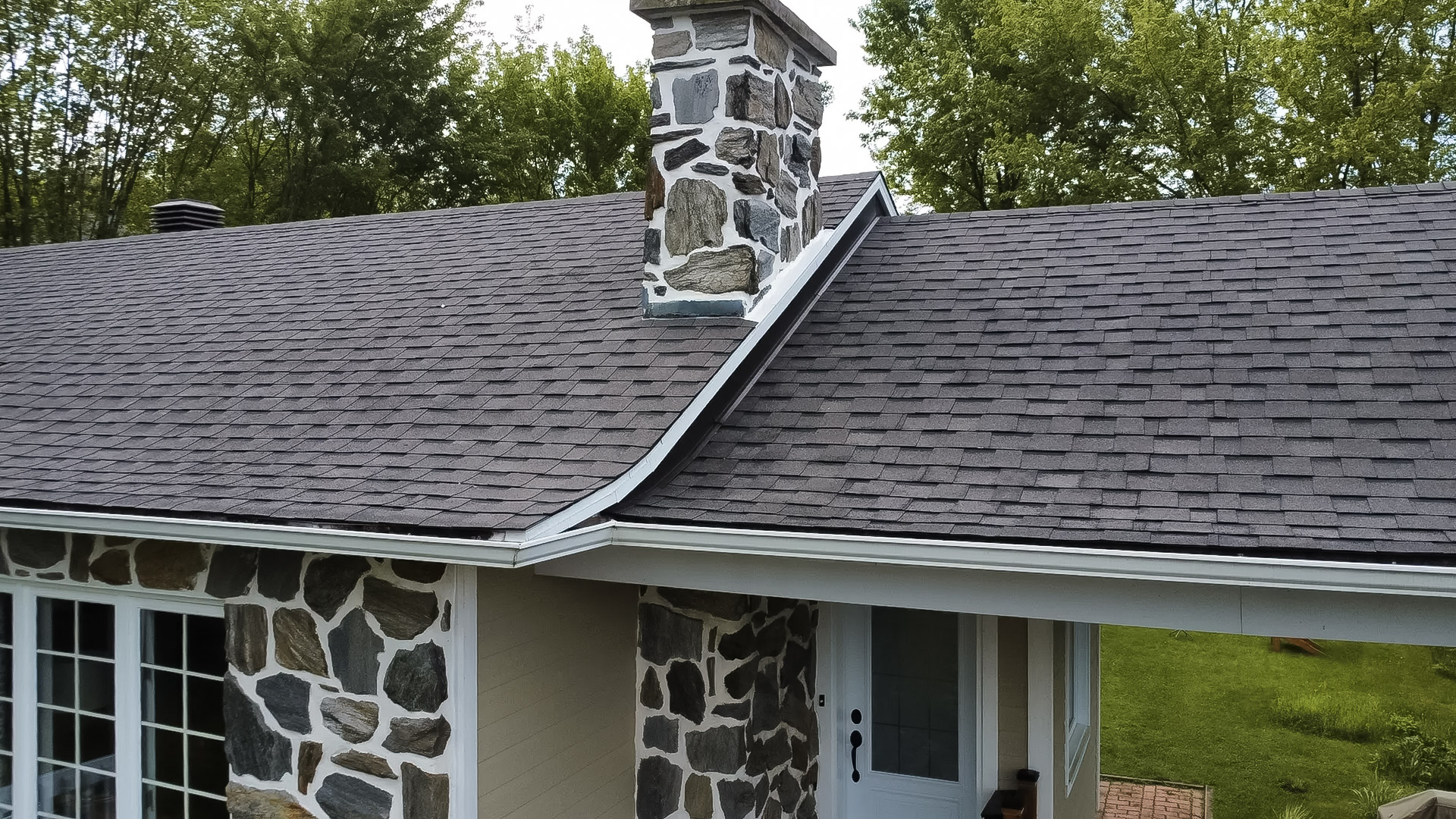 Residential roof covered with gray asphalt shingles with ventilation vents under a clear sky.