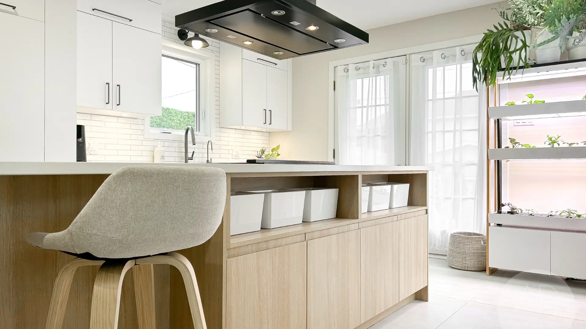 Cuisine moderne blanche et bois avec îlot multifonction, rangement ouvert, hotte noire, dosseret métro, plantes d’intérieur, chaise rembourrée et portes vitrées lumineuses