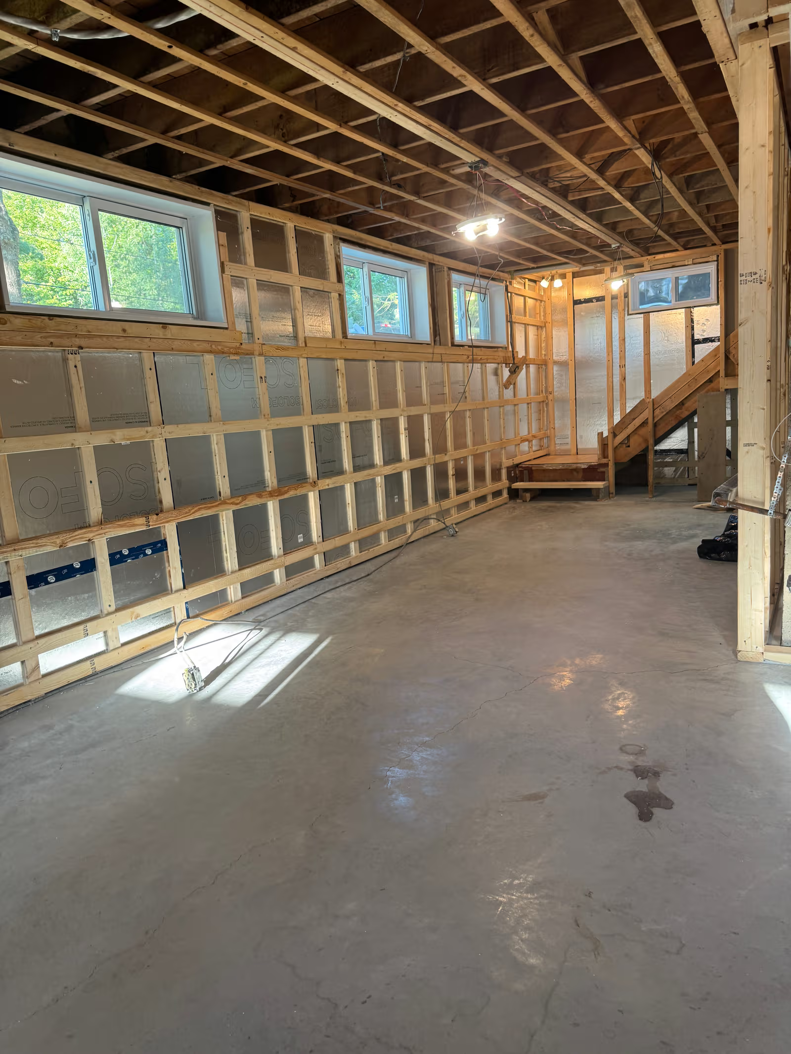Sous-sol en rénovation avec charpente apparente, isolation rigide, câblage électrique et plancher de béton