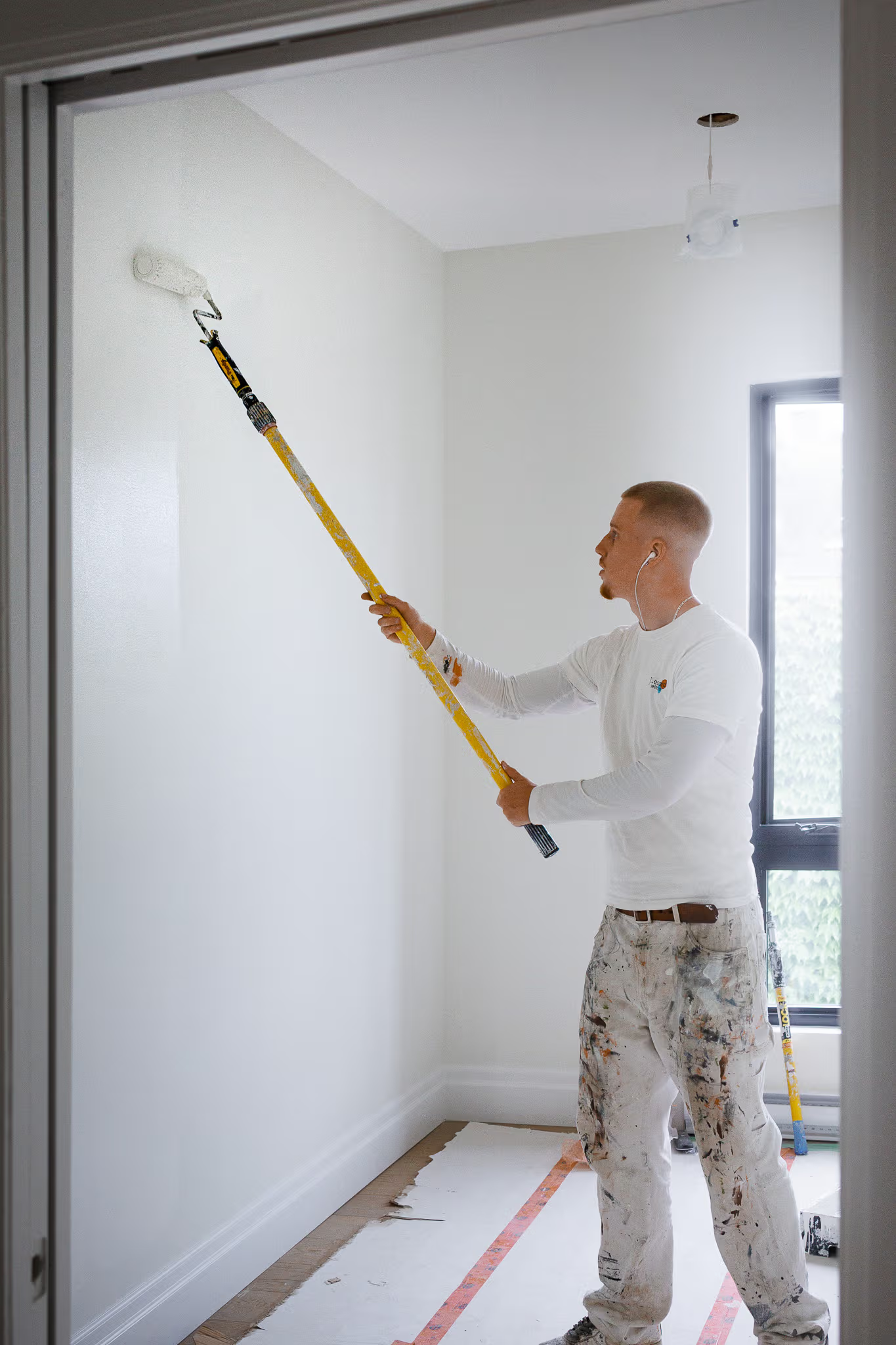 Peintre professionnel appliquant de la peinture blanche au rouleau télescopique sur un mur intérieur dans une pièce résidentielle lumineuse