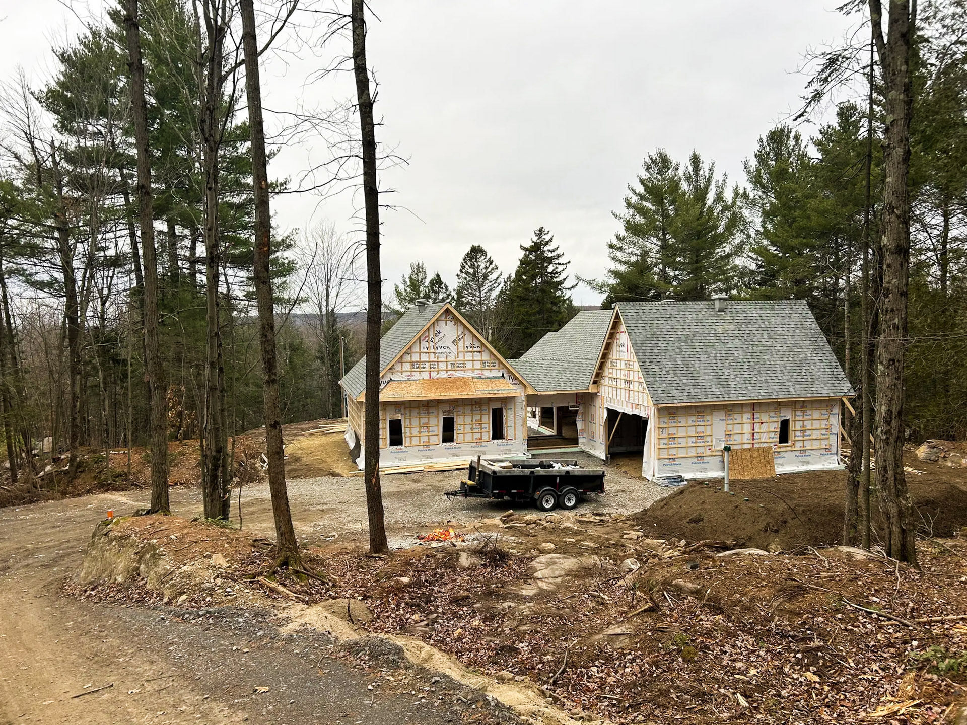 House under construction with visible frame and weather protection, located in the forest on a sloping plot