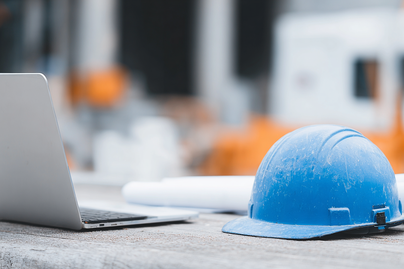 A blue hard hat placed next to a laptop on a work table.