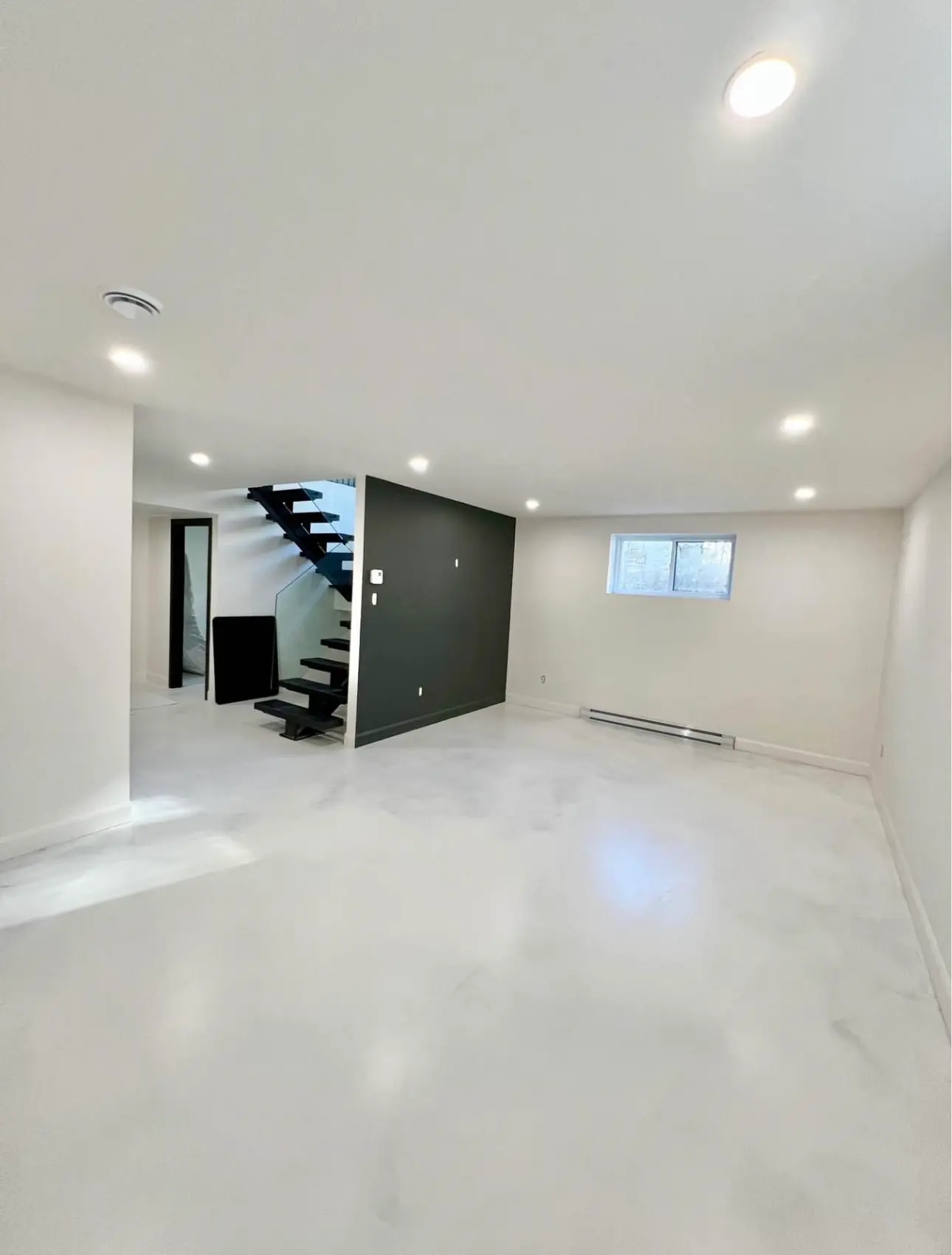 Bright renovated basement with white flooring, recessed lighting, black accent wall and modern staircase