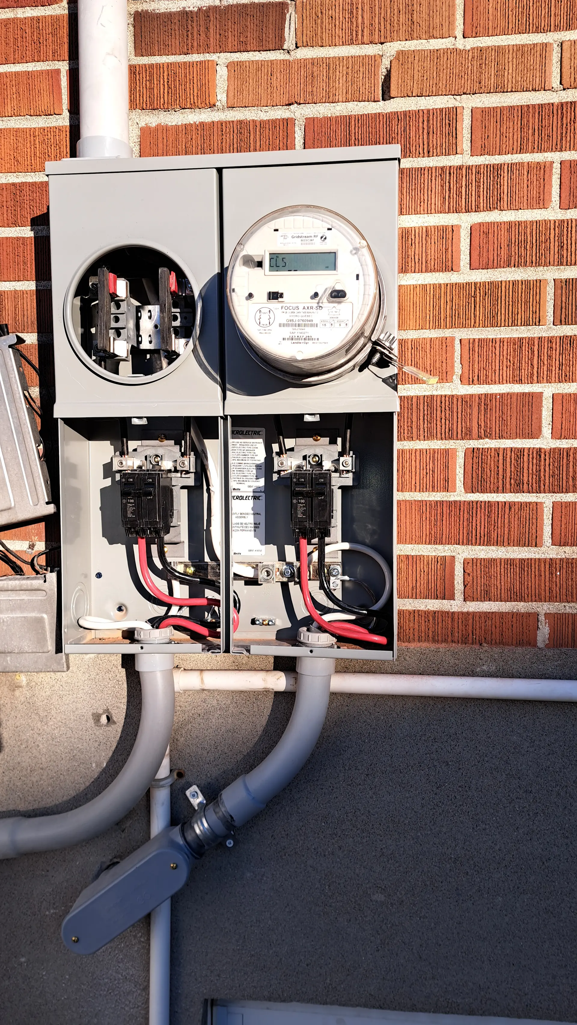 Open residential electric meter with wiring, breakers and conduits installed on an exterior brick wall