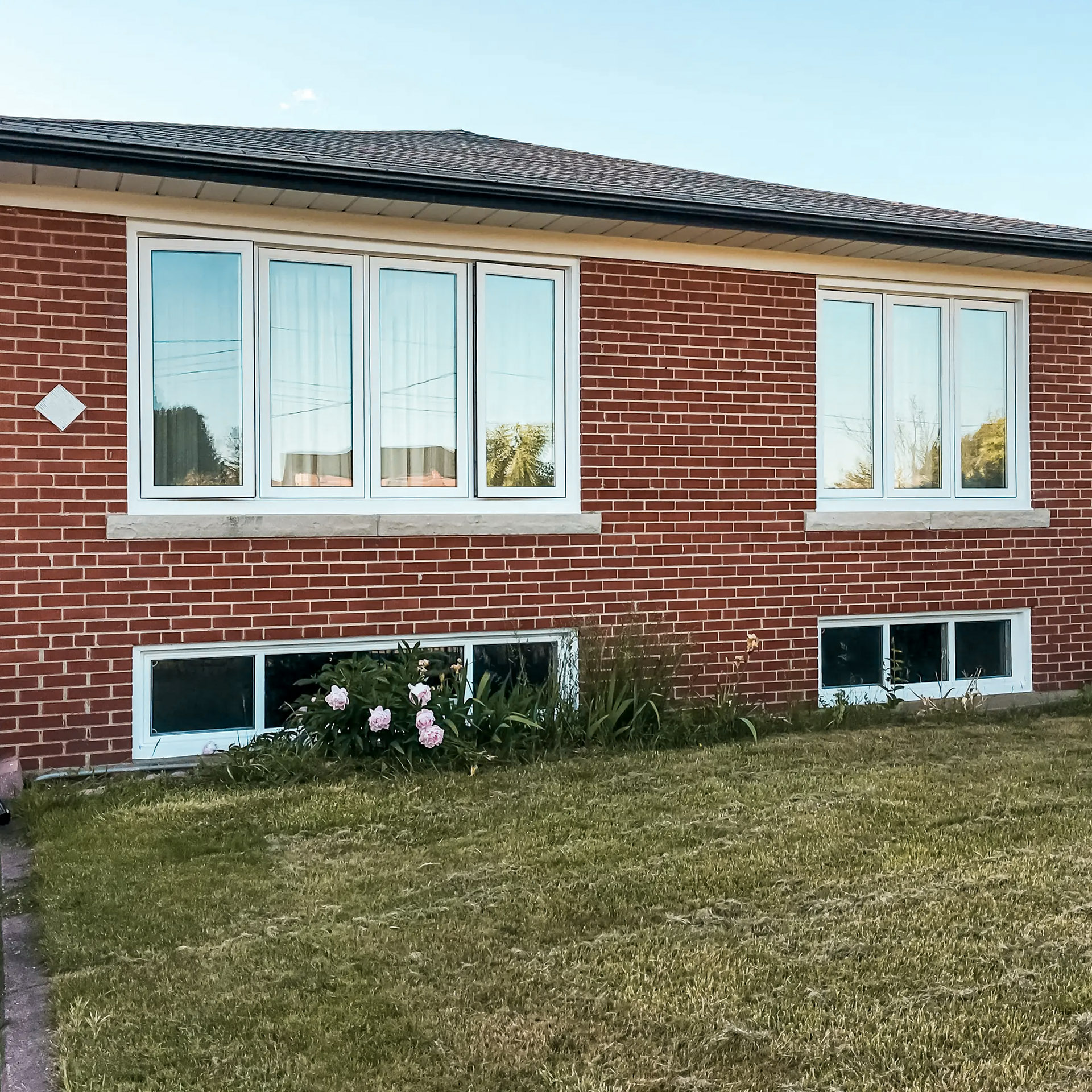 Facade of a red brick house with large modern white windows and partially visible basement