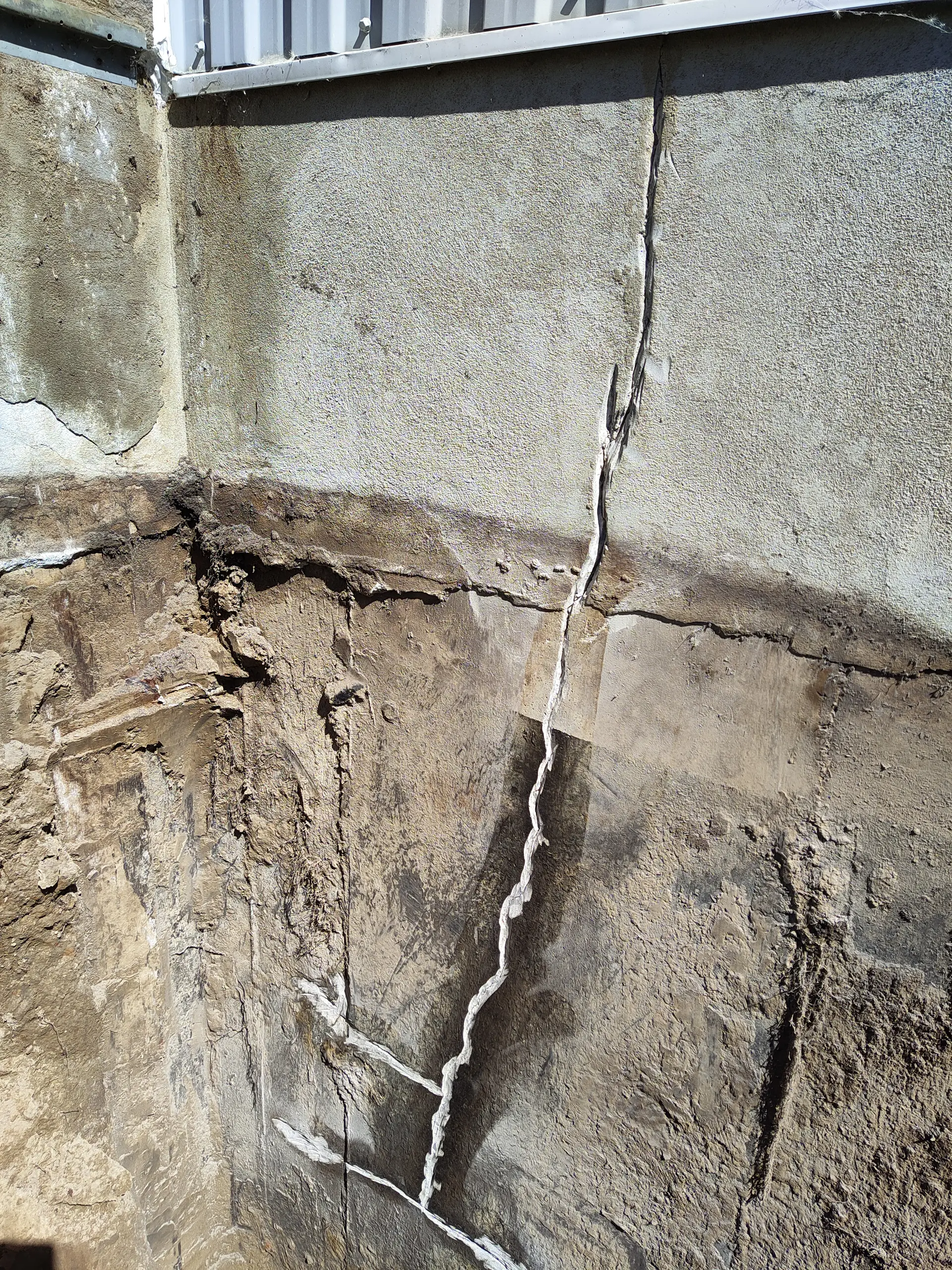 Large vertical crack in an excavated concrete foundation, with signs of previous repair and deterioration of the exterior parging.