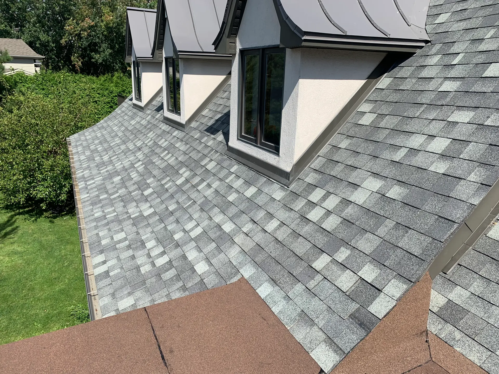 Residential roof with asphalt shingles and dormer windows overlooking a lush green garden.