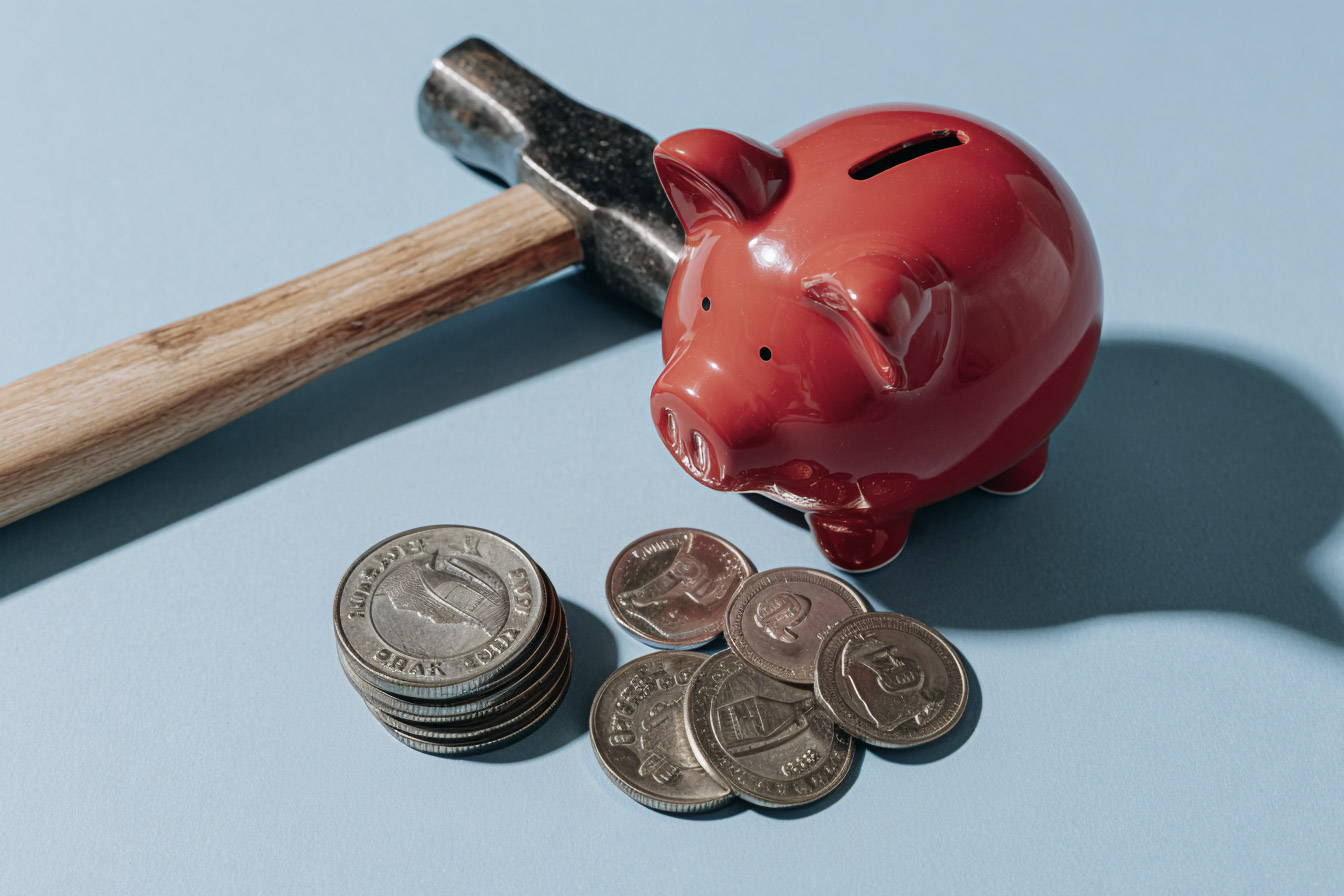 Tirelire rouge avec marteau et pièces de monnaie illustrant la gestion financière et l’épargne.