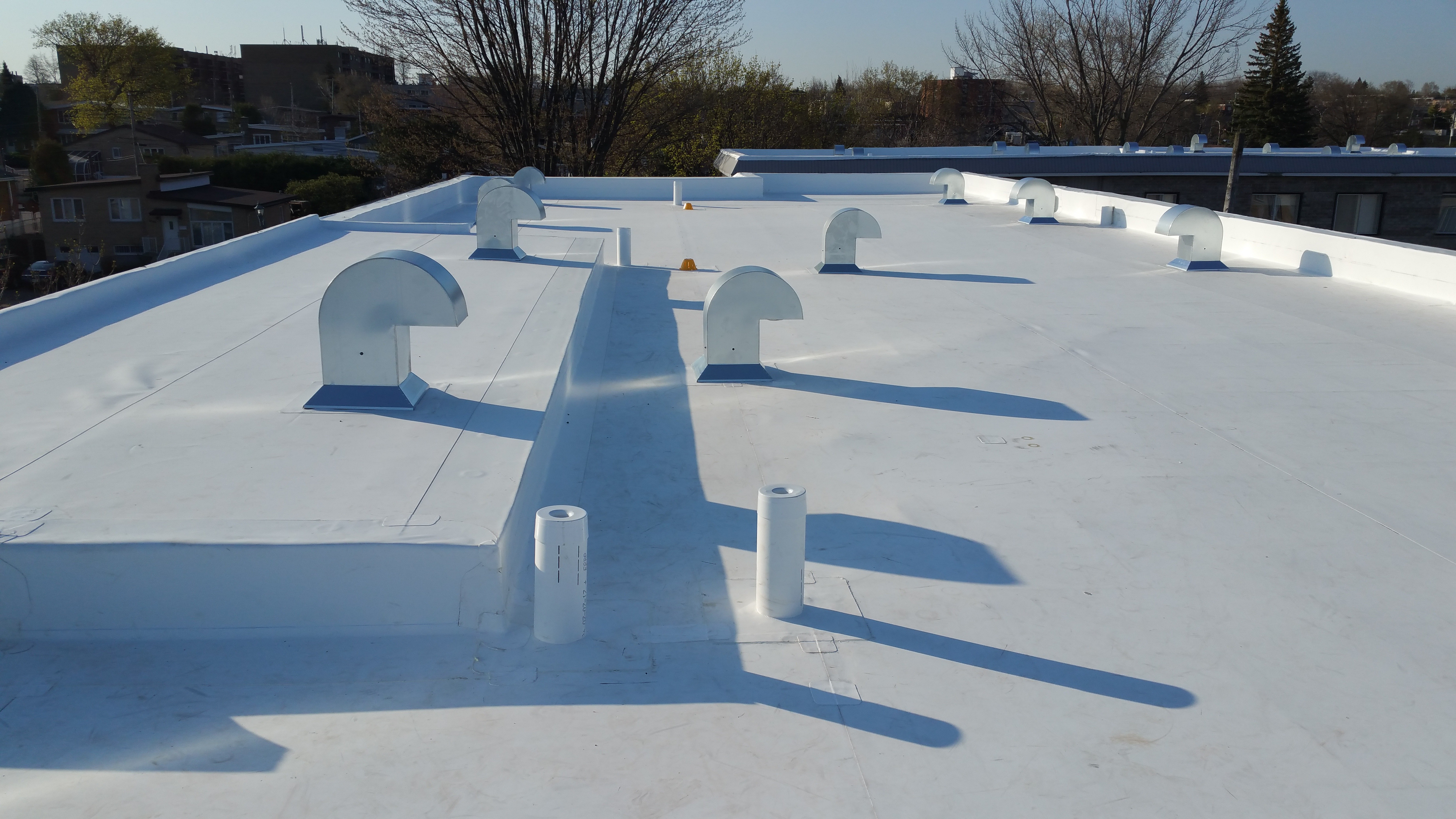 Flat roof covered with a white membrane featuring multiple metal vents and drains, ensuring waterproofing and ventilation for a residential building.