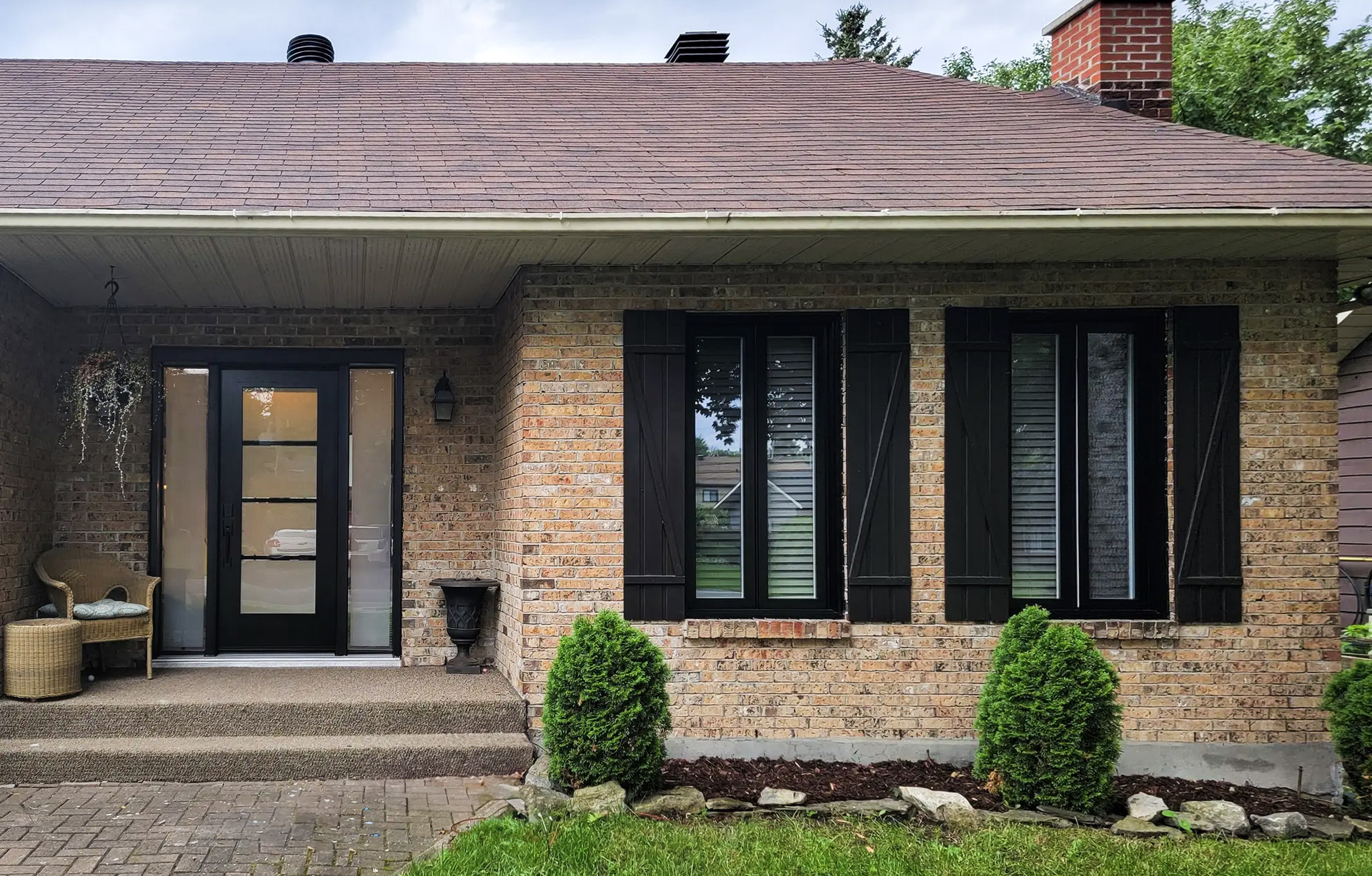Brick house with black glass door, matching shutters and small landscaping on the front.