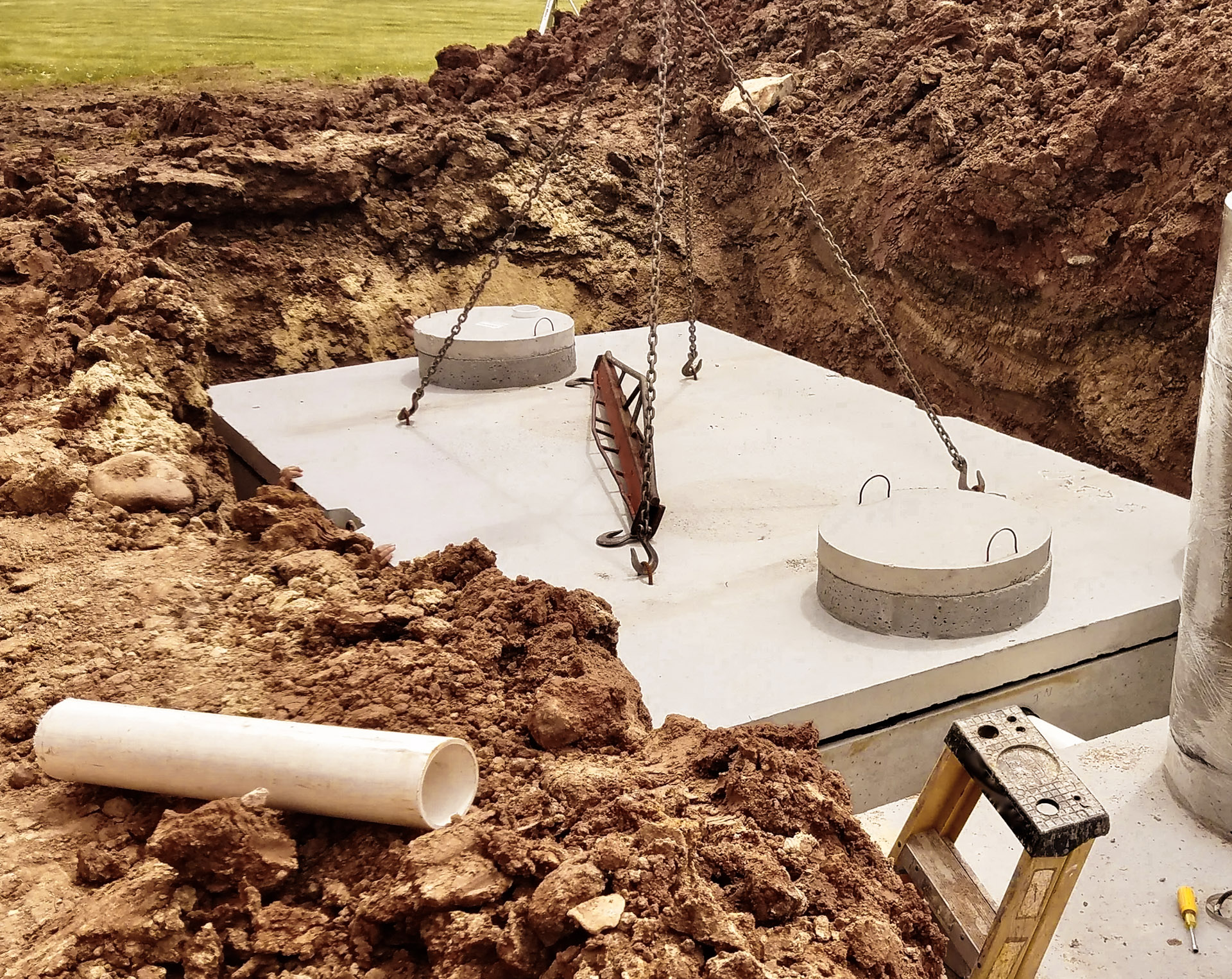 Installation of a precast concrete septic tank in an excavation, with access covers, lifting chains, and a connection pipe.