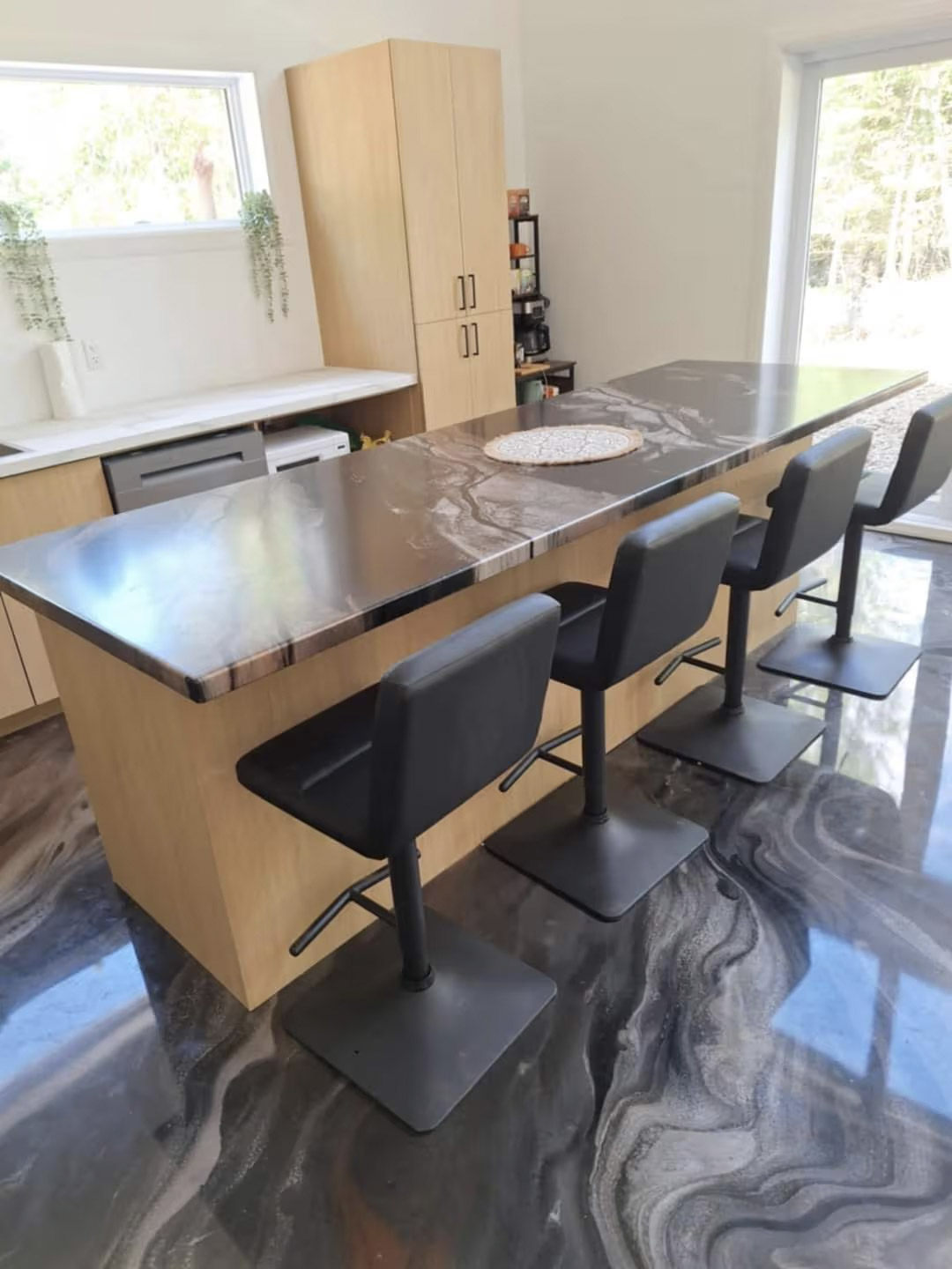 Modern kitchen with large wood island, gray marble effect countertop, black chairs and glossy patterned floor.