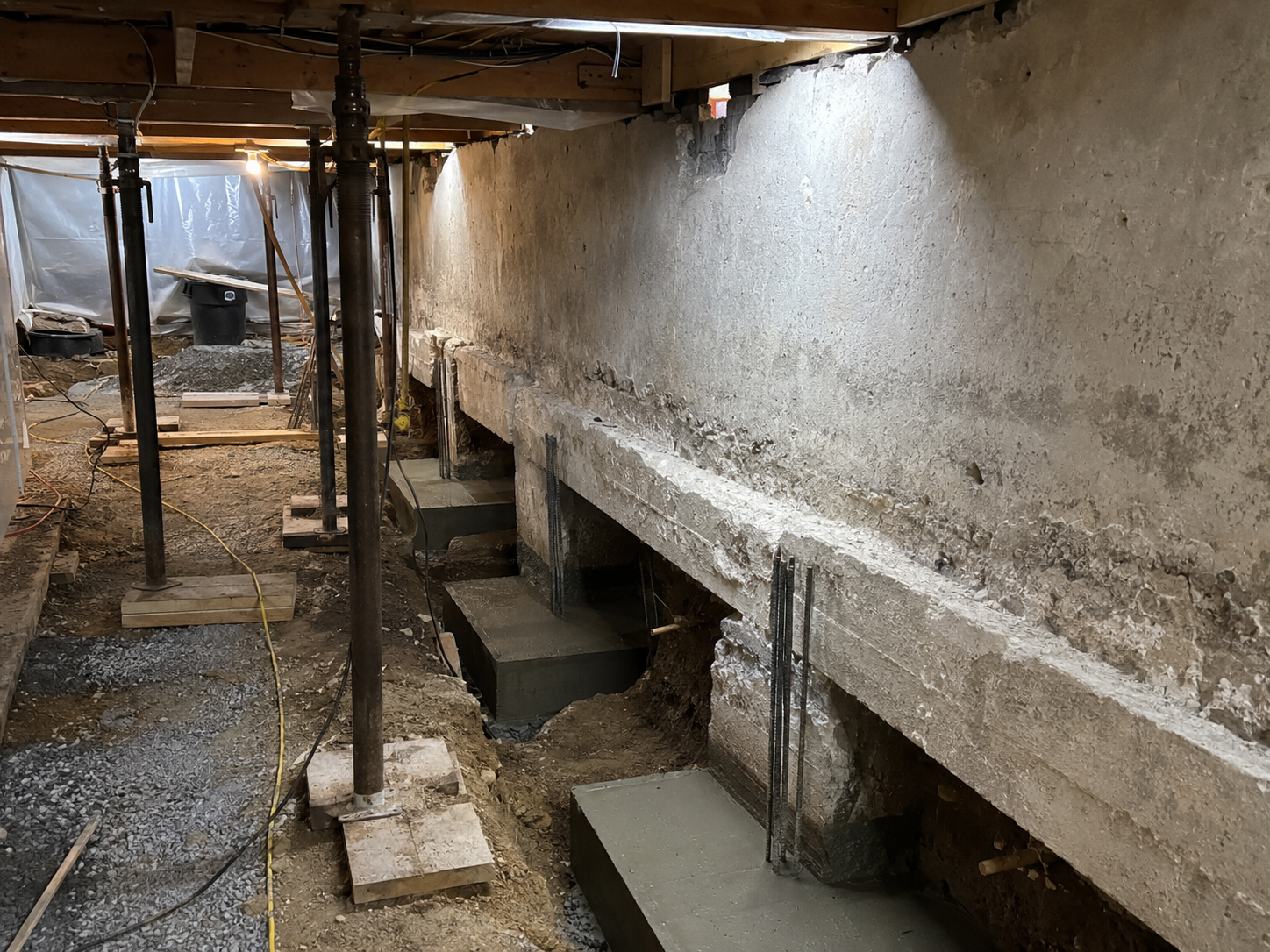 Underpinning work with sectional excavation, new concrete footings, reinforcing bars and temporary supports beneath a residential foundation