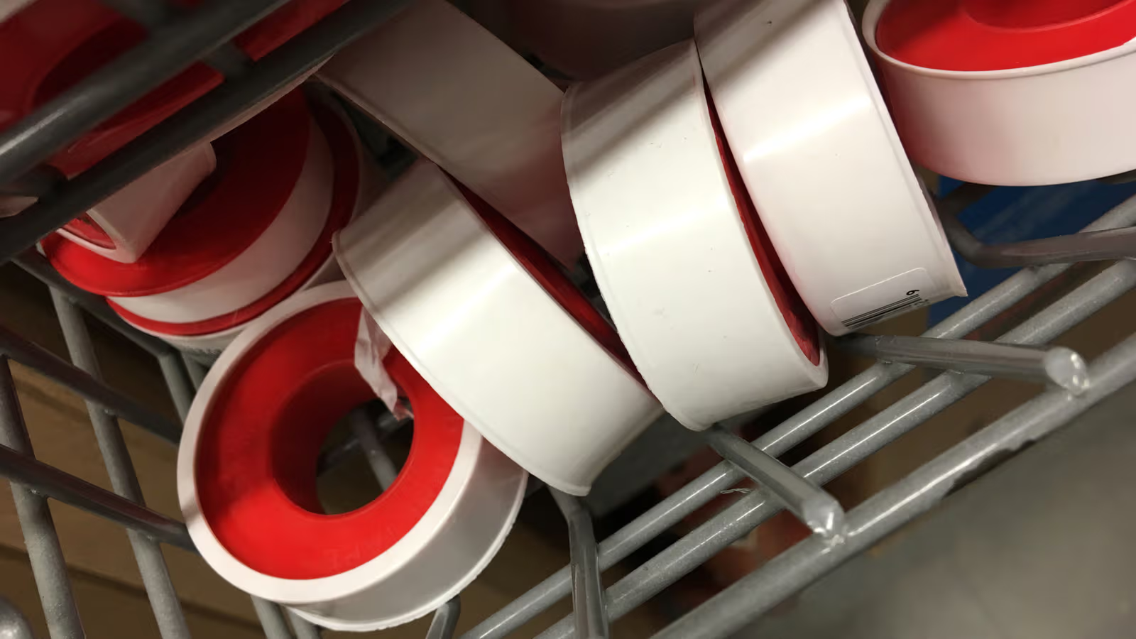 Rouleaux de ruban de plomberie blanc et rouge rangés dans un panier métallique pour travaux d’étanchéité et d’installation.