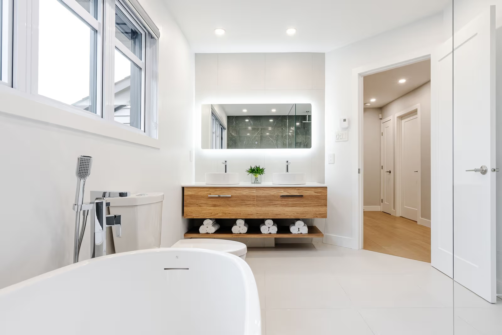 Salle de bain contemporaine lumineuse avec double vasque en bois, miroir rétroéclairé et baignoire moderne