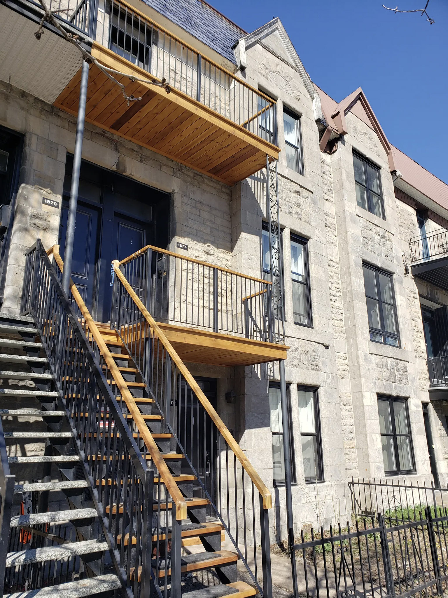 Facade of a stone plex in Montreal with exterior metal and wood stairs leading to renovated balconies