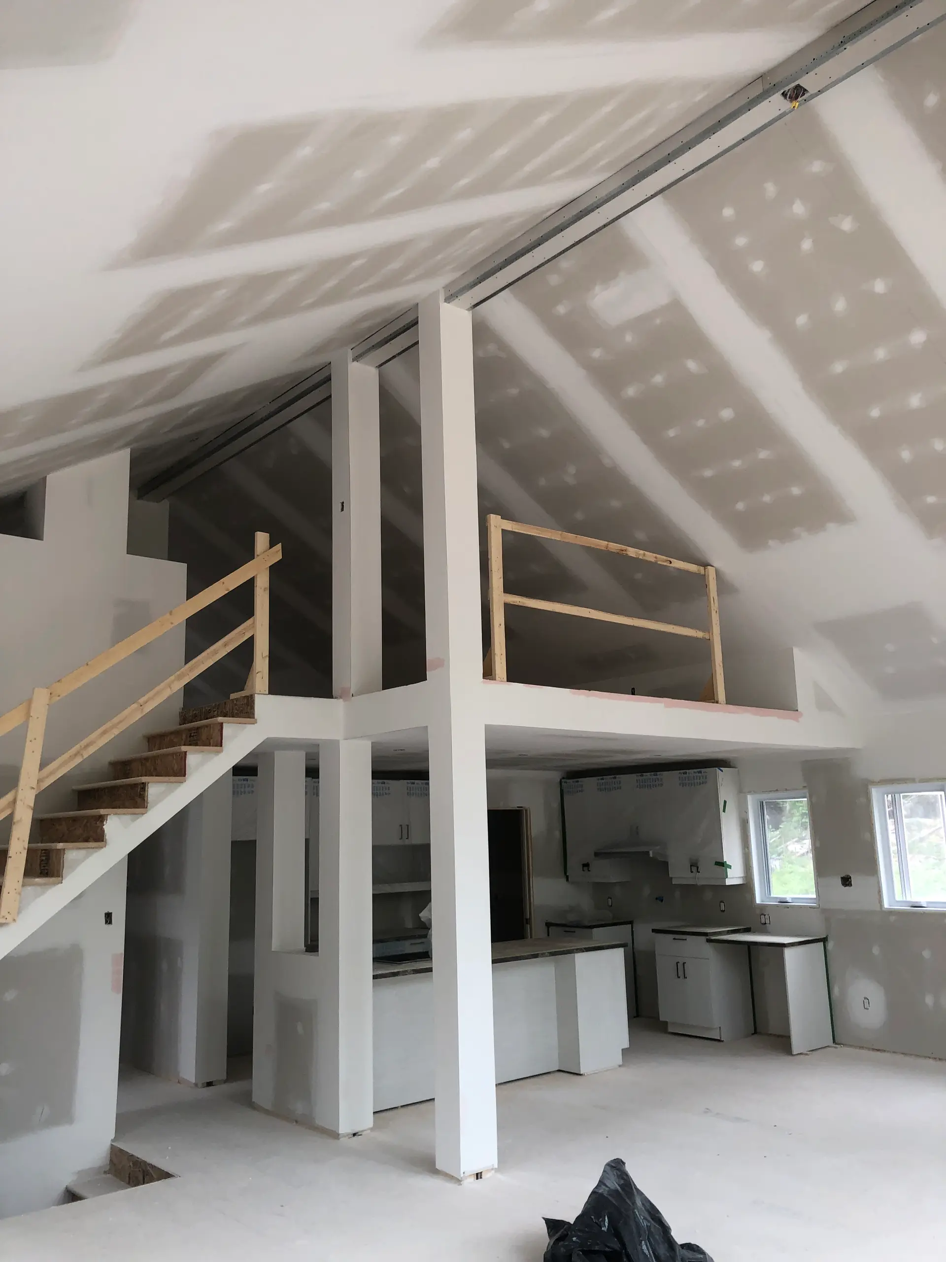 Interior under renovation with taped cathedral drywall ceilings, a mezzanine, temporary staircase, and kitchen installation in progress.