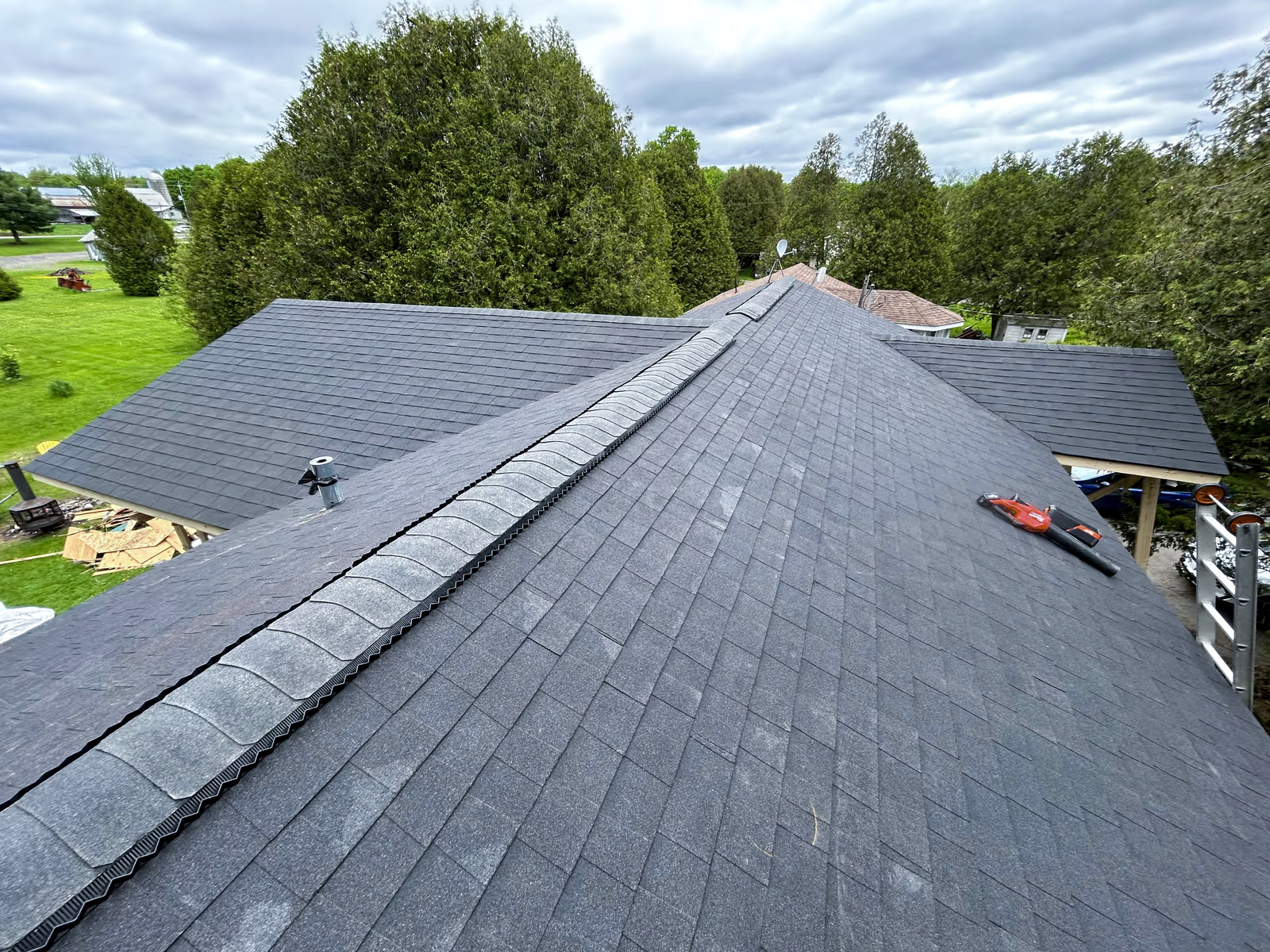 Newly installed residential roof with grey asphalt shingles, illustrating renovation or construction work in a wooded setting.