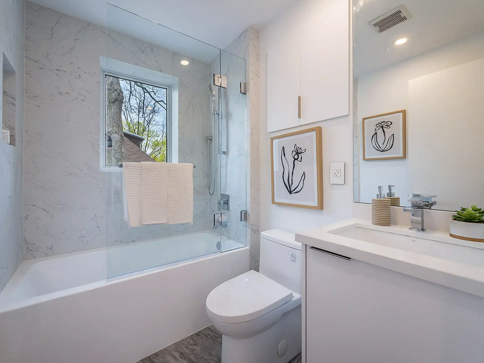 Salle de bain moderne avec baignoire-douche vitrée, vanité blanche et carrelage effet marbre lumineux