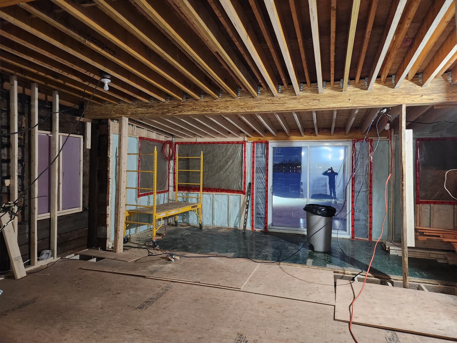 Home interior under major renovation with exposed framing, insulation, wiring and patio door