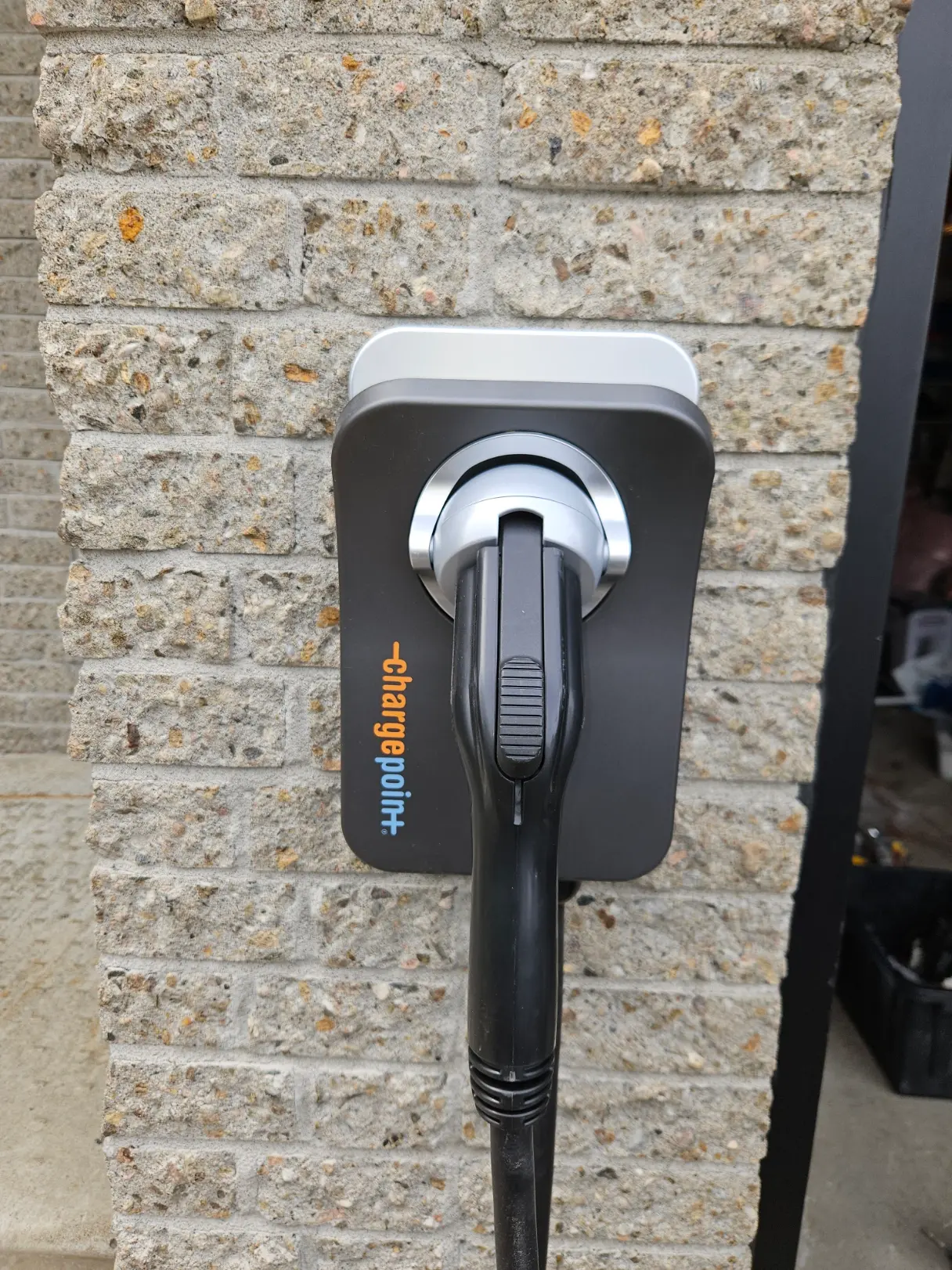 Borne de recharge électrique murale noire avec connecteur branché sur façade en brique extérieure