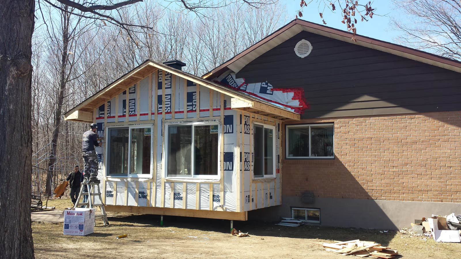 Agrandissement de maison en construction avec charpente en bois, fenêtres installées, pare-air, toiture et revêtement extérieur à compléter
