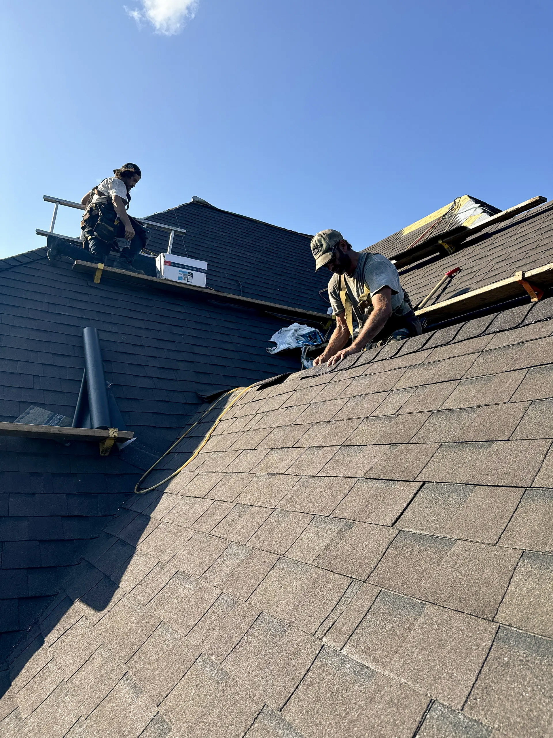 Travailleurs sur un toit en pente effectuant des travaux de couverture avec des bardeaux d’asphalte sous un ciel dégagé