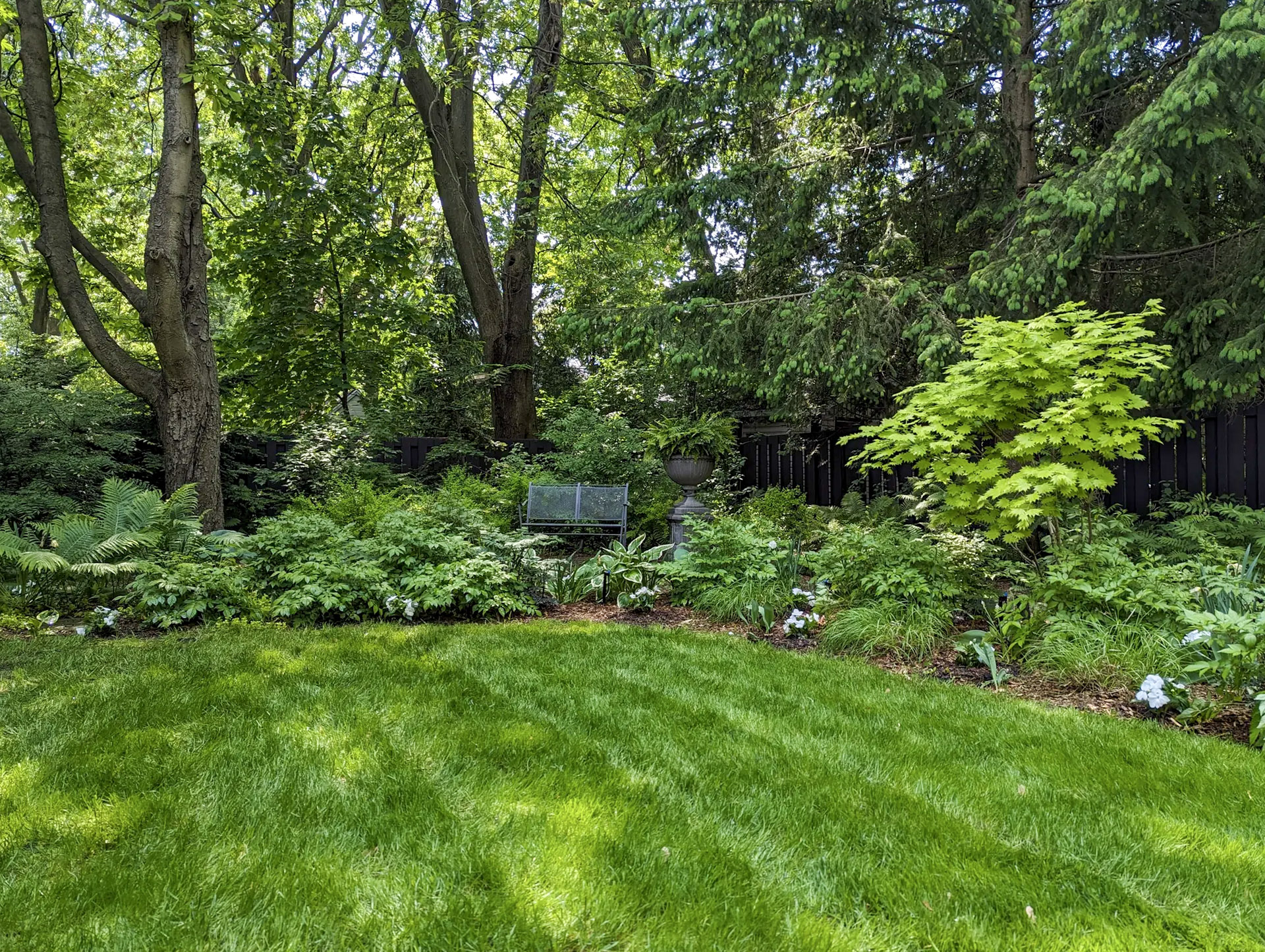 Jardin luxuriant avec pelouse bien entretenue, arbres matures et coin détente ombragé