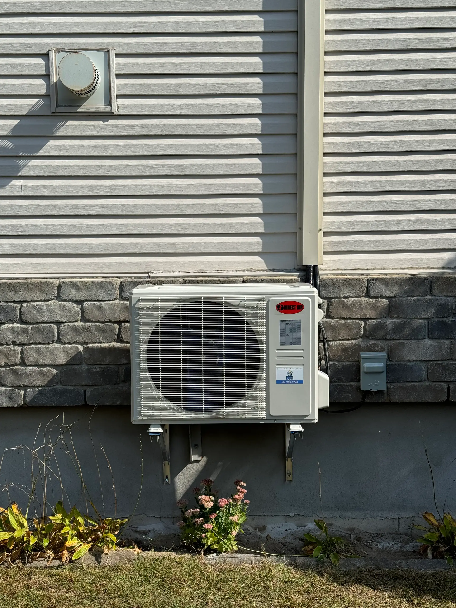 Thermopompe murale extérieure de marque Direct Air installée sur un mur de maison en pierre et vinyle