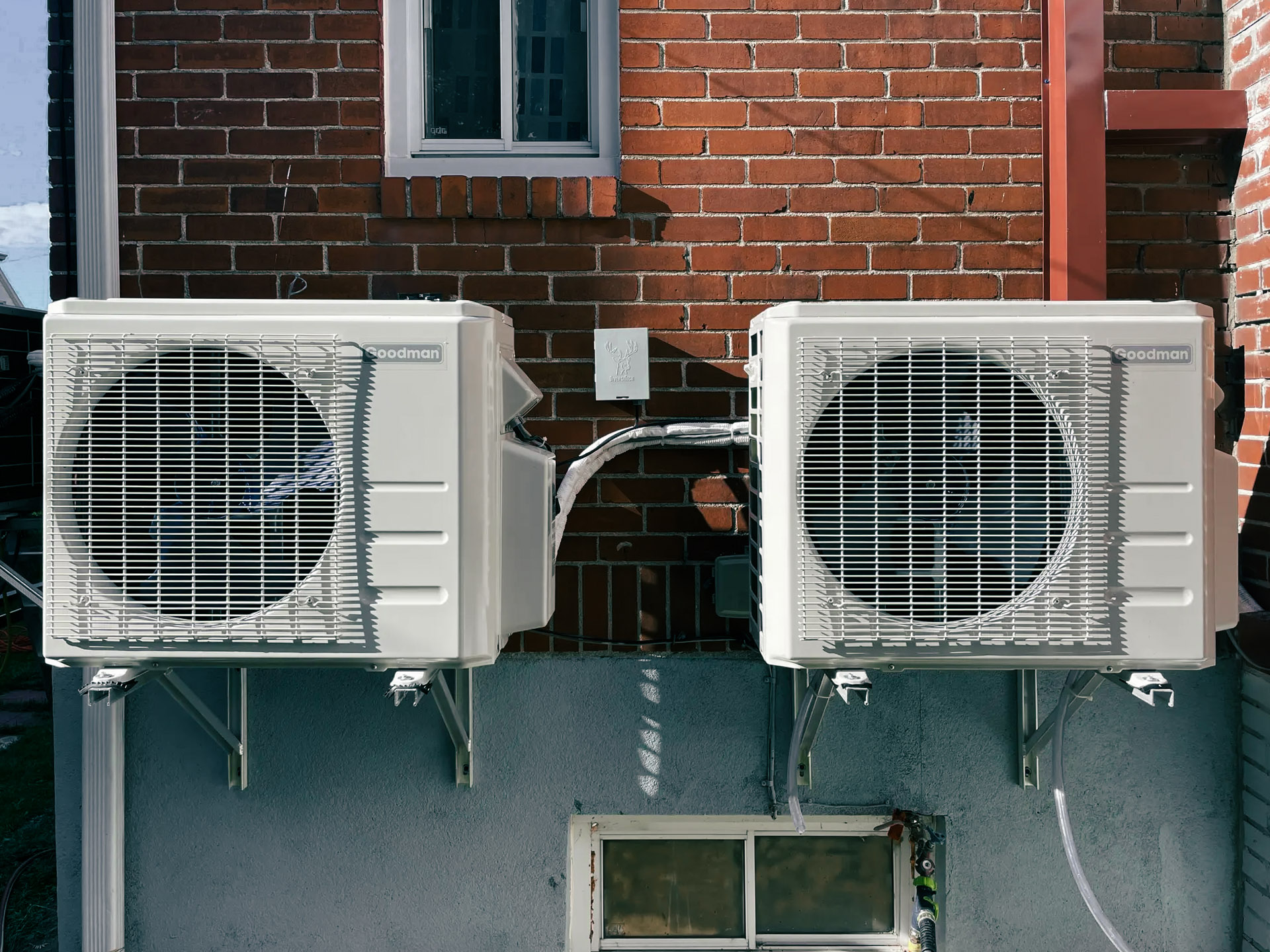 Installation of two outdoor wall-mounted heat pump units on metal brackets attached to a residential brick exterior wall.