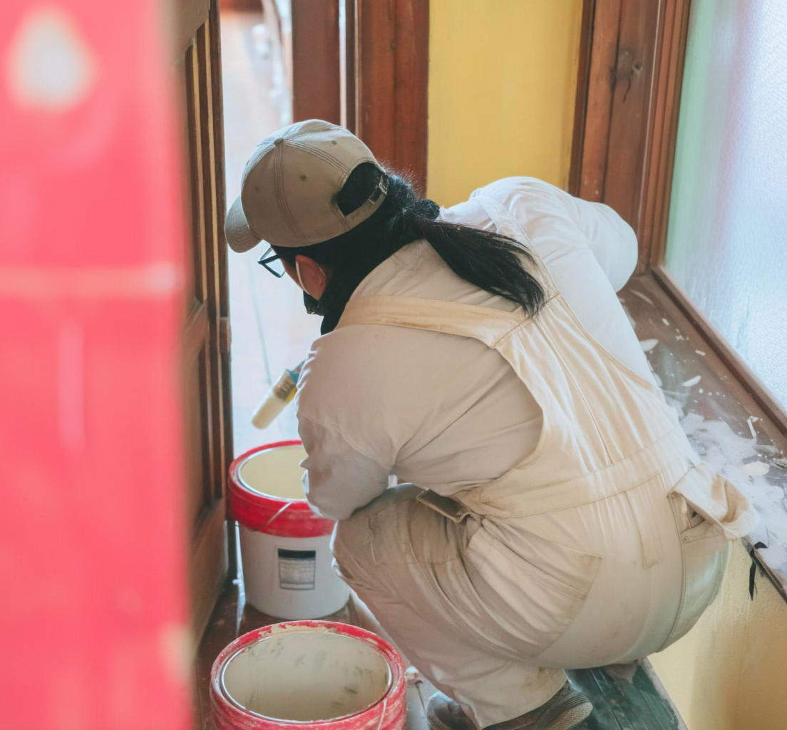 Peintre en combinaison blanche préparant de la peinture blanche dans un seau à l’intérieur d’une maison