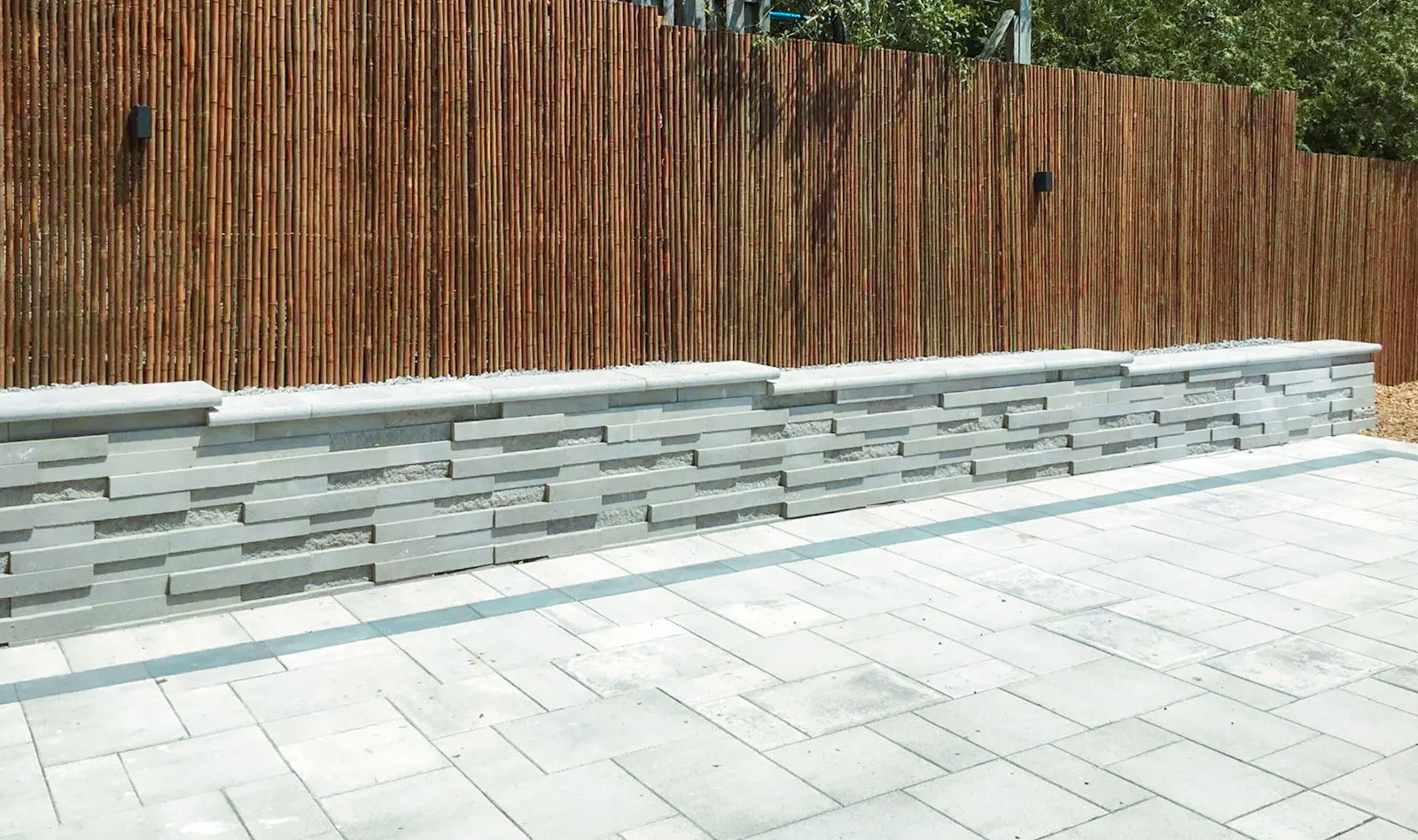 Modern gray concrete block wall with paving stone patio and vertical wood fence