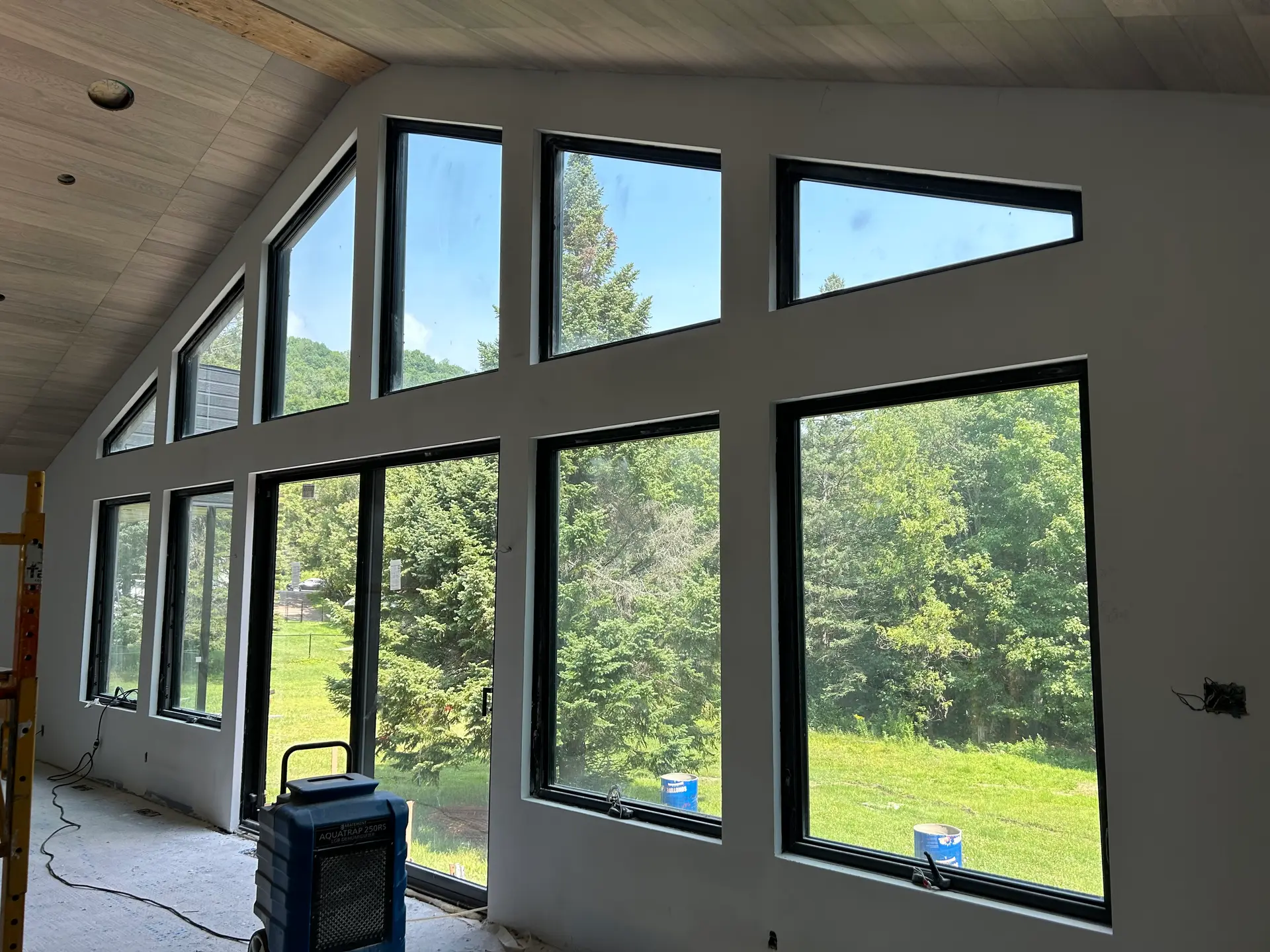 Intérieur d'une maison en construction avec une grande façade vitrée offrant une vue panoramique sur la nature.
