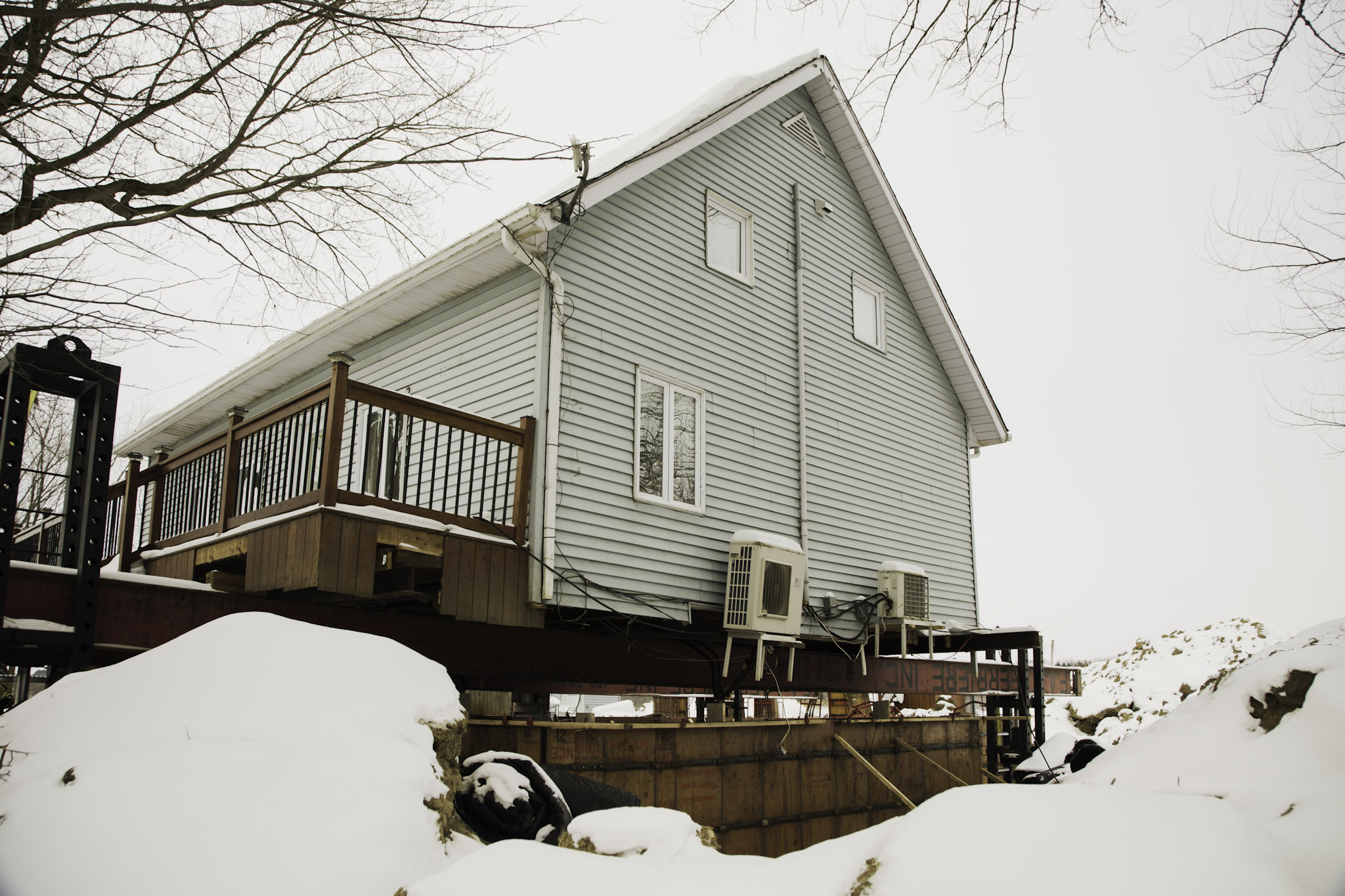 Maison surélevée en hiver avec coffrage de fondation visible et unités de thermopompe murale installées.