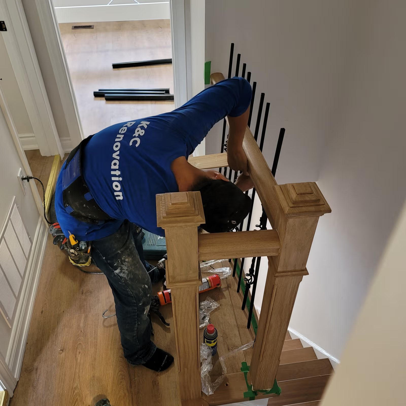 Installer fitting a wooden stair railing with black balusters in a home renovation project
